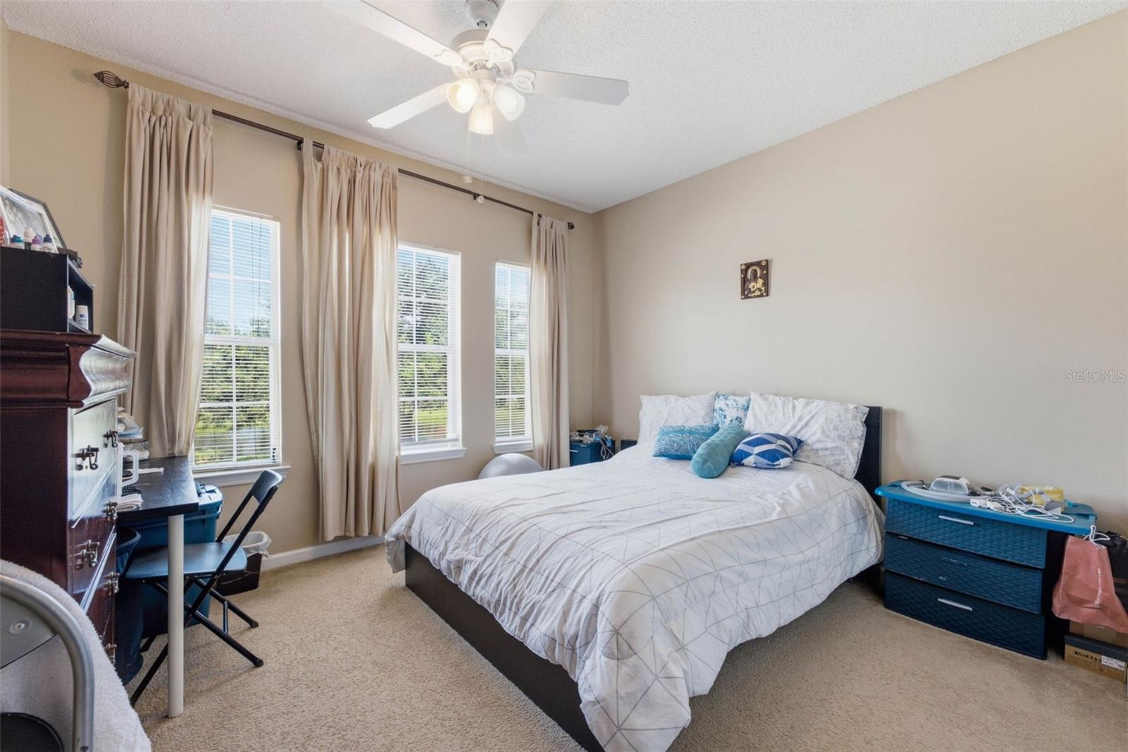 Furnished bedroom with a large bed, three curtained windows, and beige carpet.