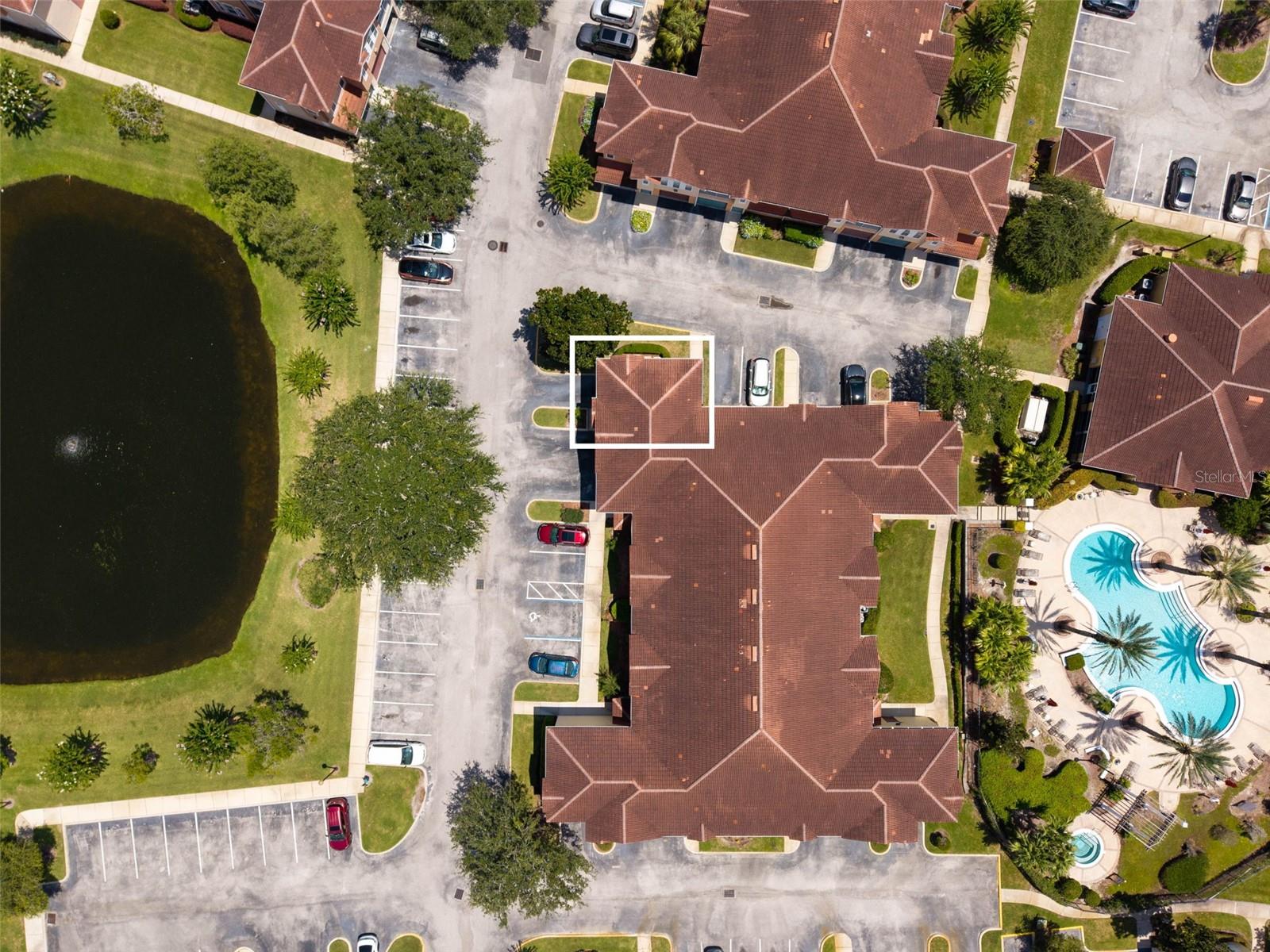 Aerial view of a condominium complex, with one unit outlined beside parking, a pond, and a pool.