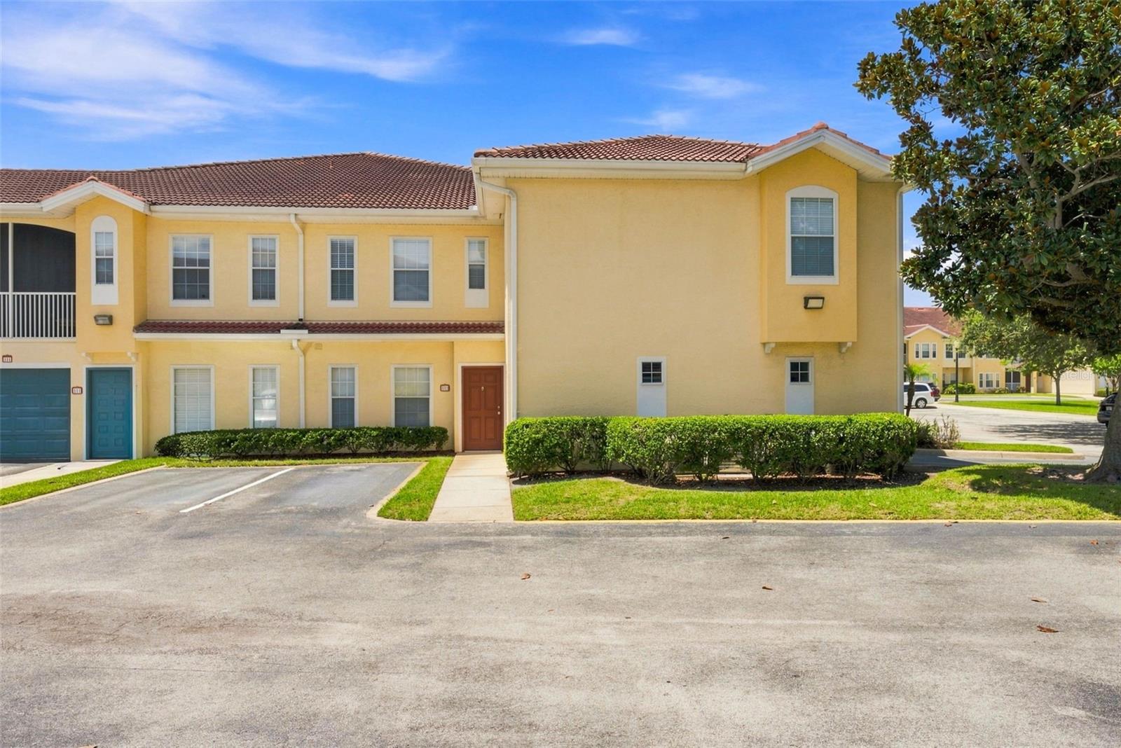 Yellow two-story townhouse with a tiled roof, front walk, and neatly trimmed hedges.