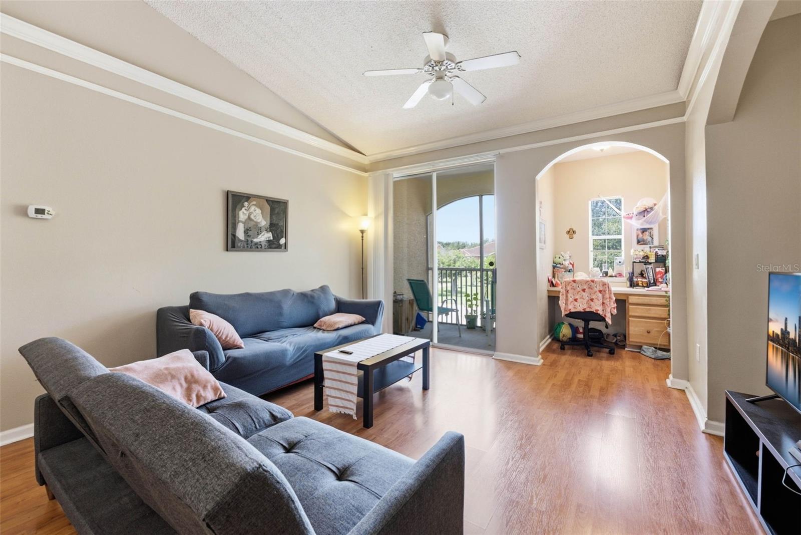 Living room with gray sofas, sliding doors to a balcony, and an arched opening to a desk nook.