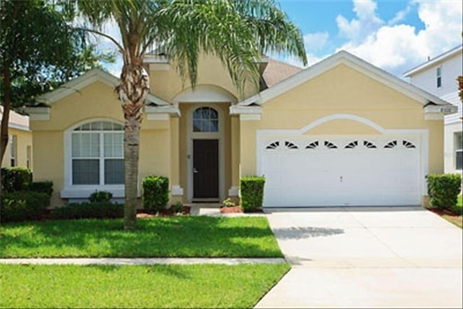 Yellow stucco home with a white double garage, arched entry, and palm tree in front.