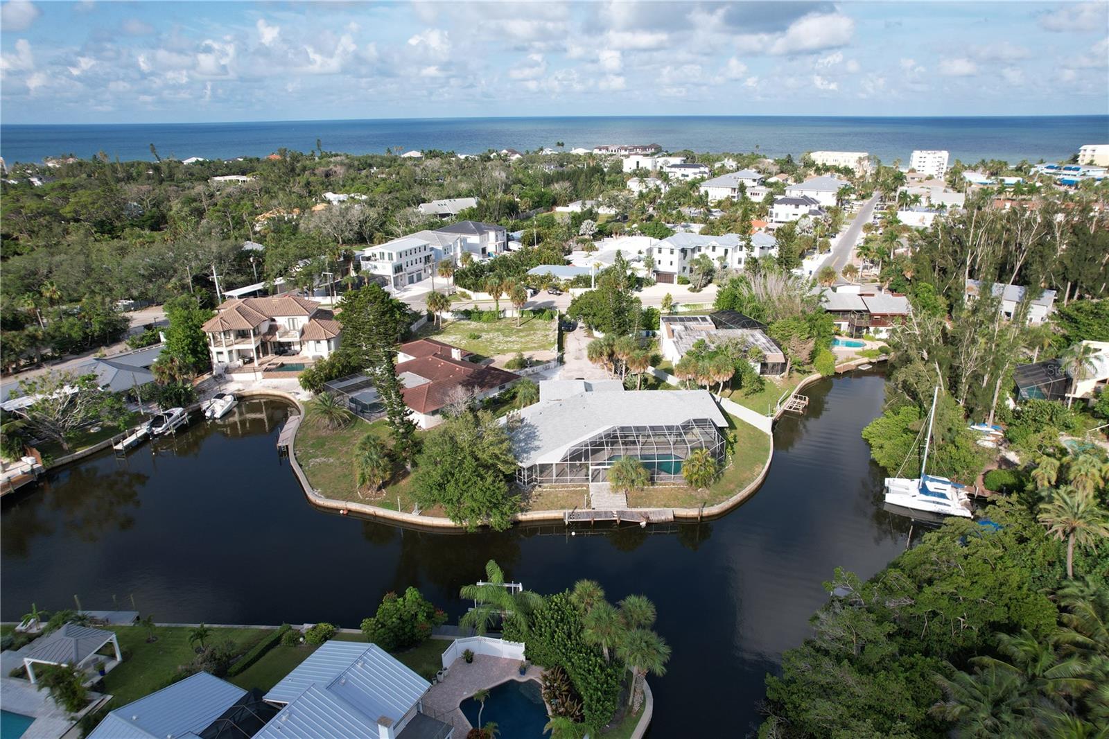 Aerial view of a canal-front home with a screened pool and the ocean beyond.