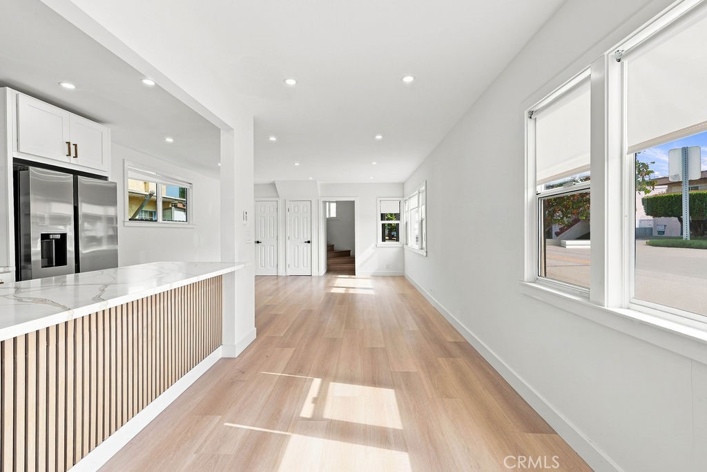 Bright open kitchen with a marble-look island, stainless steel refrigerator, and light wood floors.