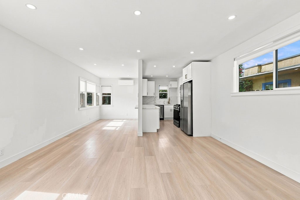 Open kitchen and living area with light wood floors, white cabinetry, and stainless steel appliances.
