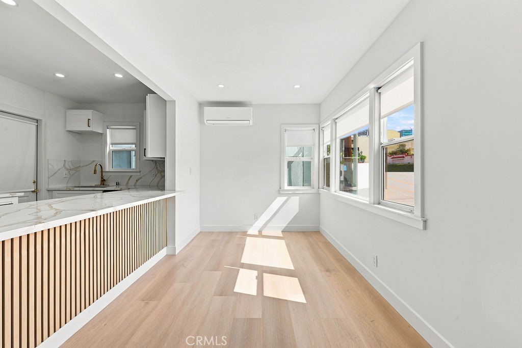 Bright unfurnished living area with large windows, light wood floors, and a slatted kitchen peninsula.