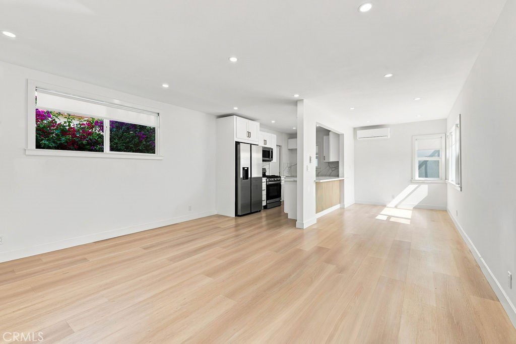 Vacant open-plan living area with light wood floors and a compact kitchen with stainless steel appliances.