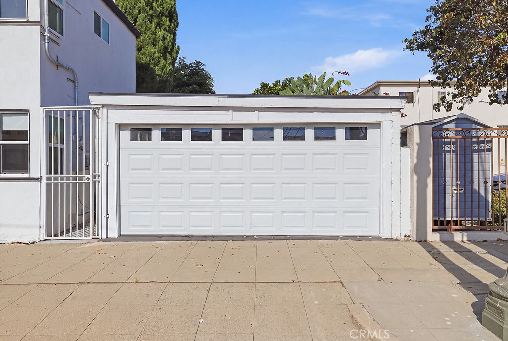 White double garage door with upper windows, flanked by metal gates along a concrete sidewalk.