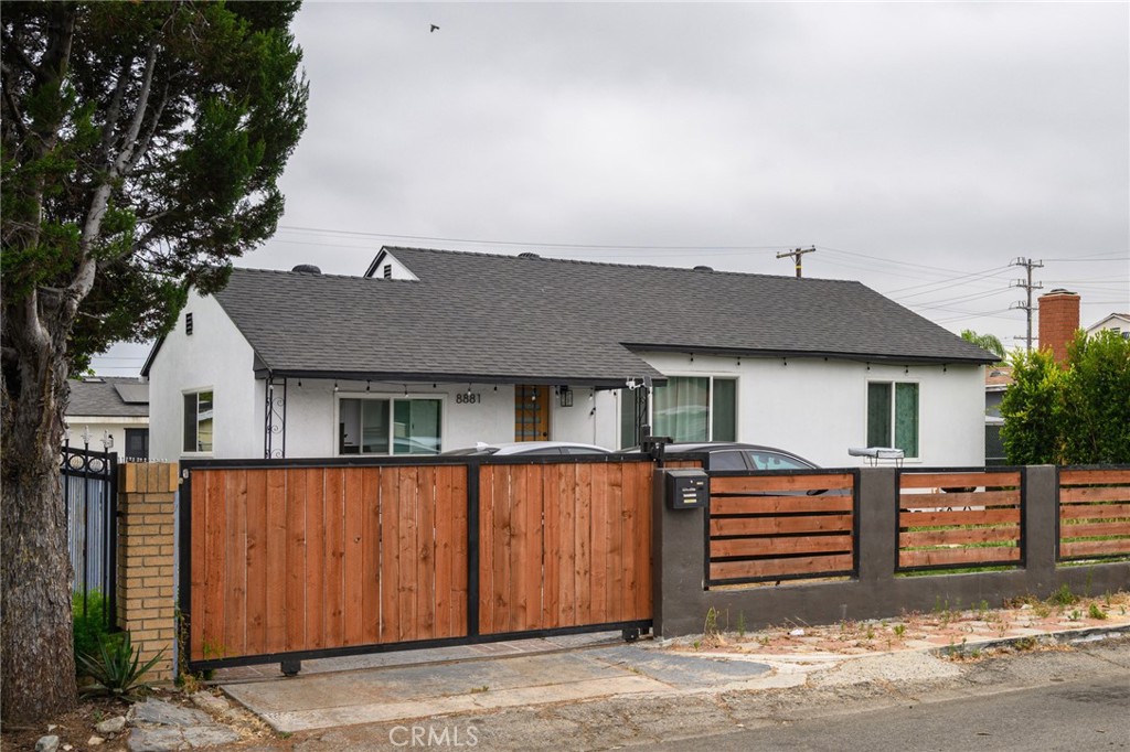 White single-story house behind a tall wood-and-black-metal fence, with a car parked inside.