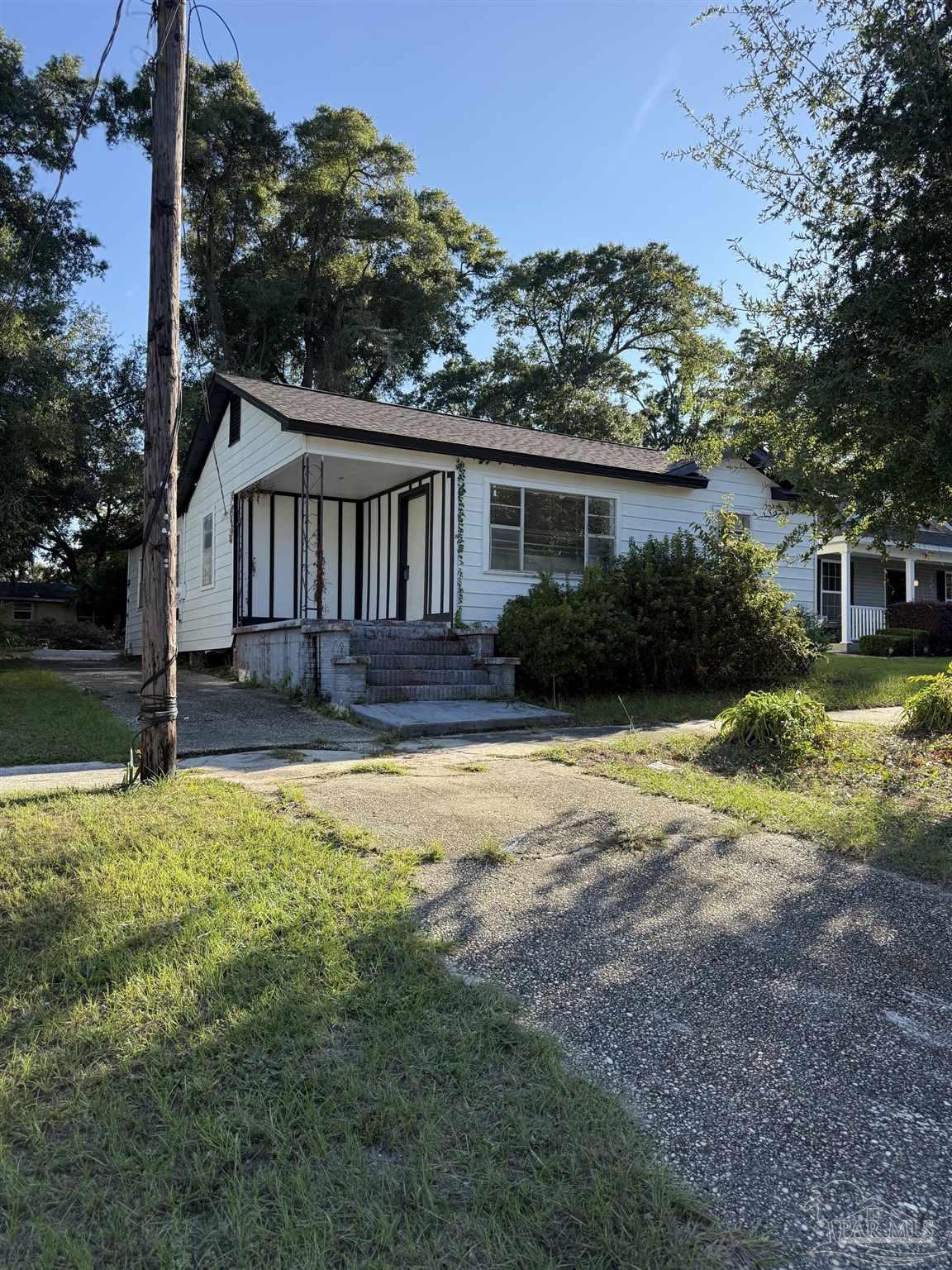 White single-story house with a covered porch, concrete steps, and a broad gravel driveway.
