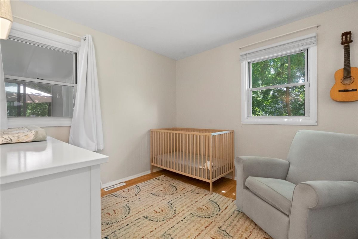 Nursery with a wooden crib, gray armchair, and patterned rug.