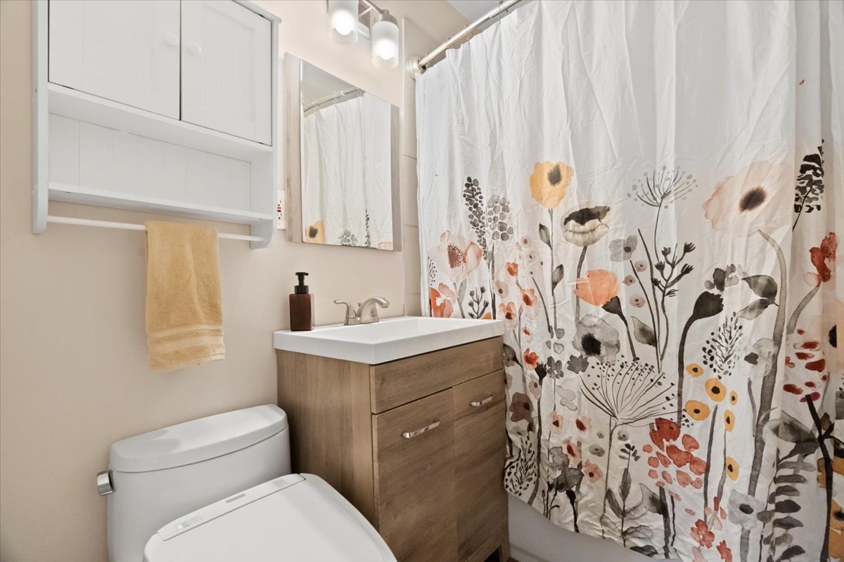 Bathroom with wood vanity, toilet, mirrored cabinet, and floral shower curtain.