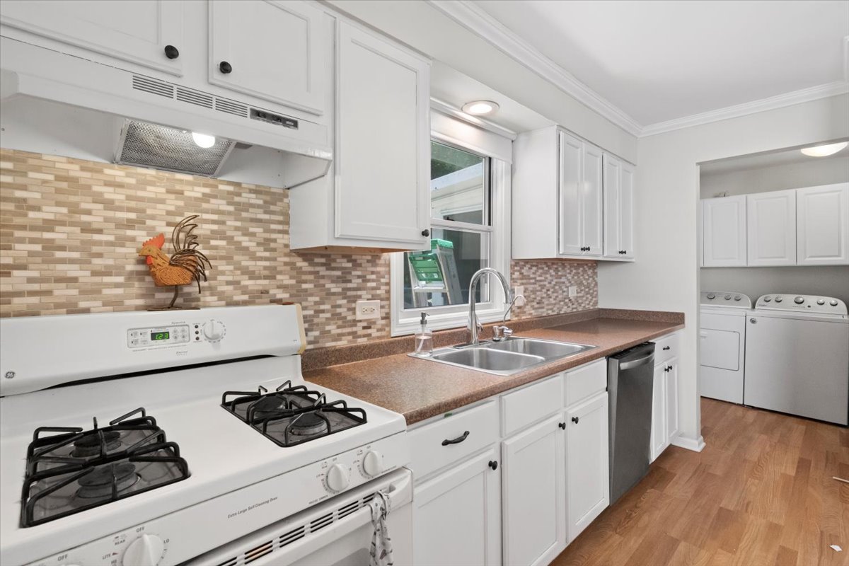 Kitchen with white cabinets, a gas range, mosaic tile backsplash, and washer and dryer in the adjoining laundry area.