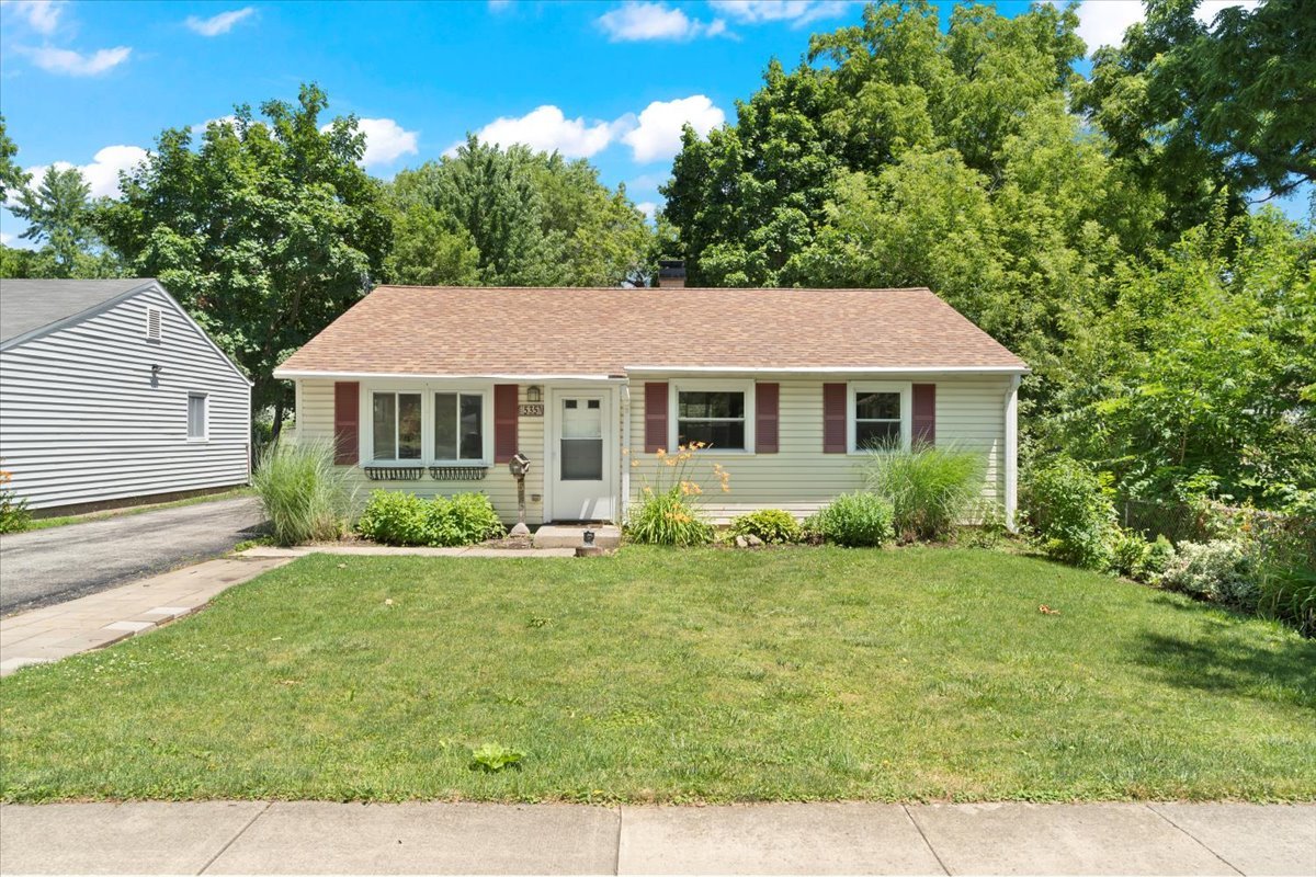 Single-story house with burgundy shutters, a broad front lawn, and mature trees.