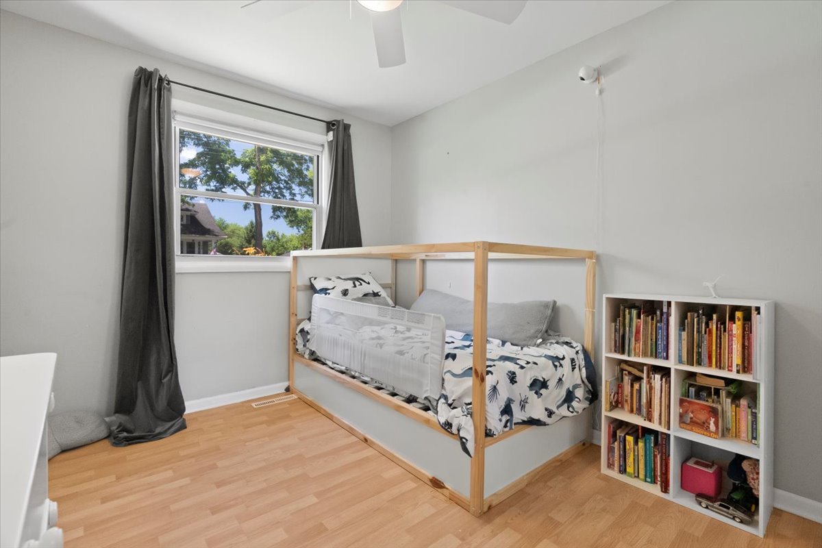 Bedroom with a wooden-framed bed, dinosaur-print bedding, and a bookcase of children’s books.