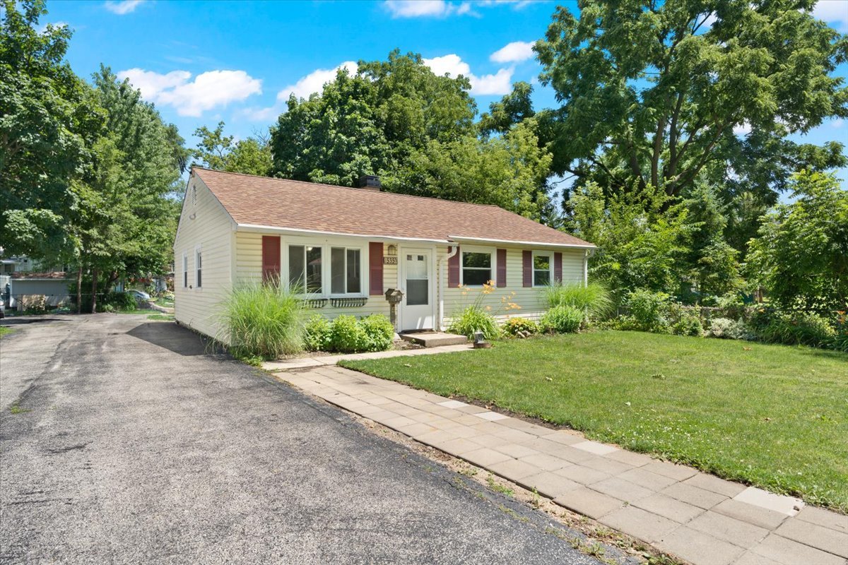 Single-story cream house with red shutters, a paved driveway, and a walkway through the front lawn.