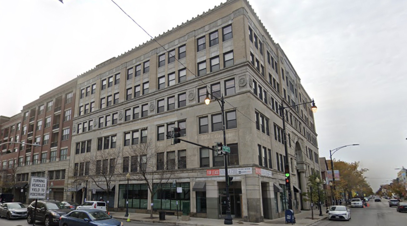Multi-story stone building on a city corner with storefronts and autumn trees.