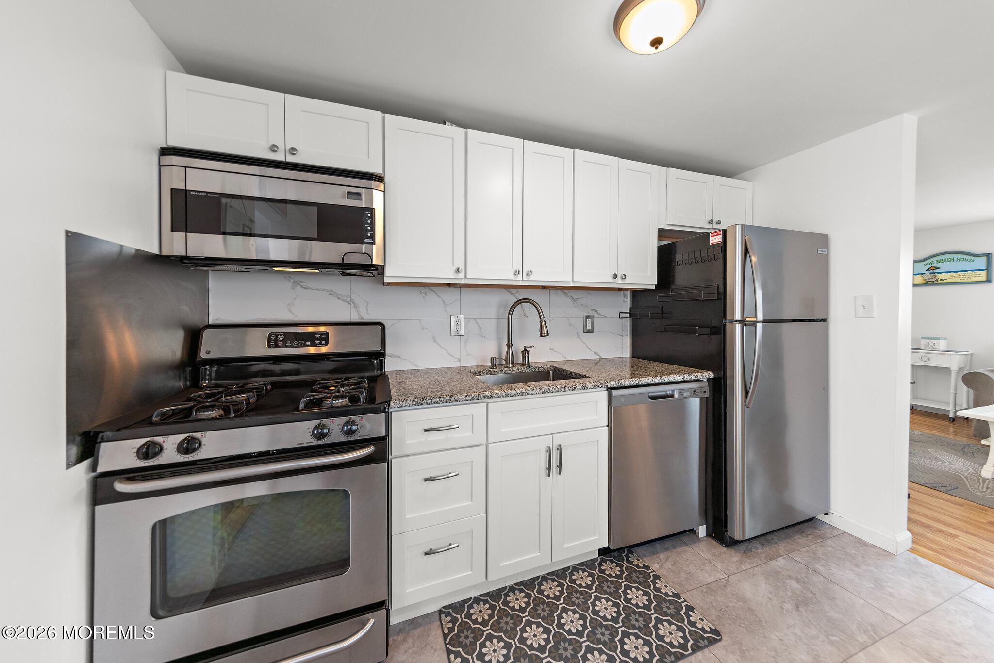 Kitchen with white cabinets, stainless steel appliances, granite counters, and a patterned floor mat.