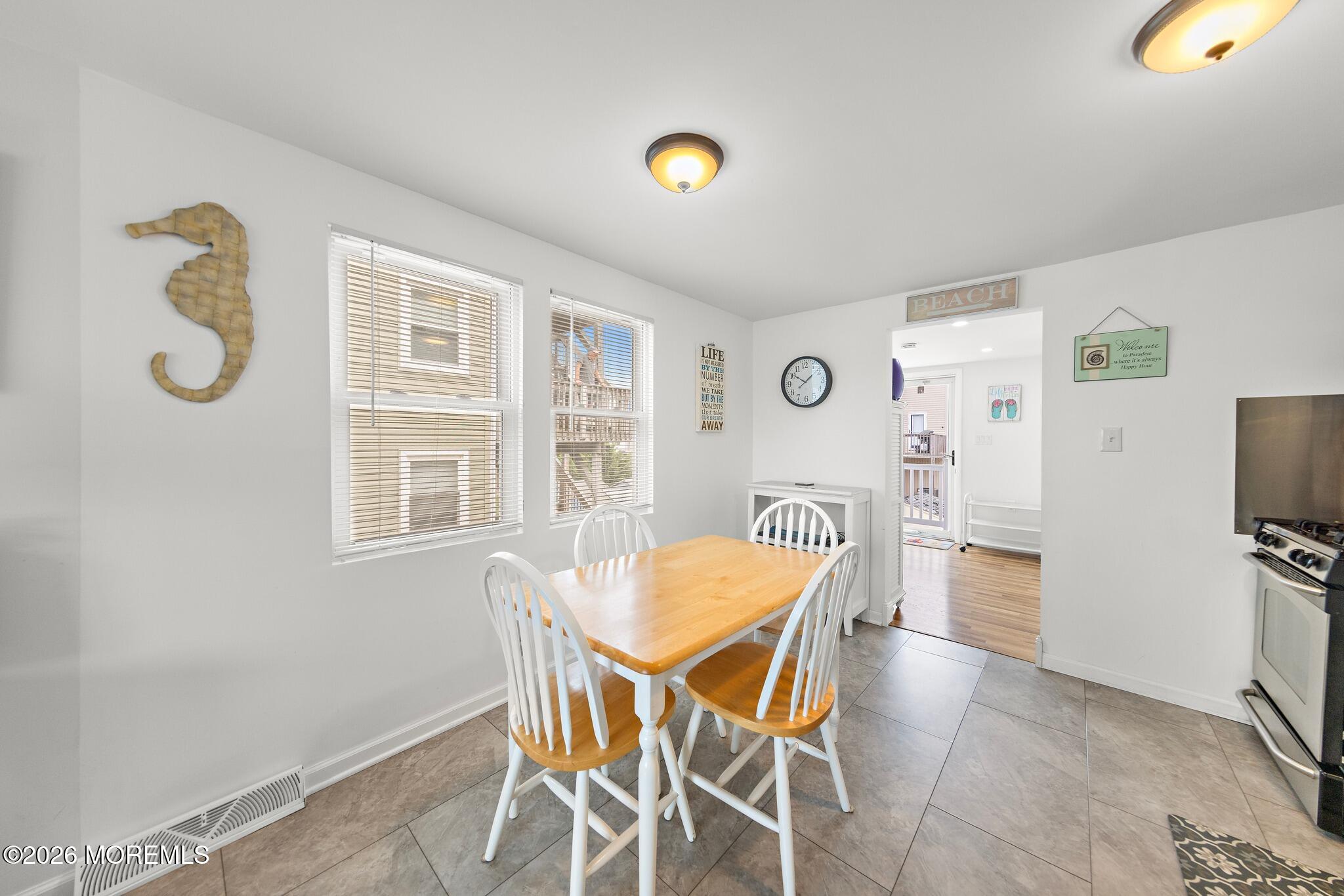 Dining area with a wood-top table, white chairs, tiled floor, and coastal decorations.