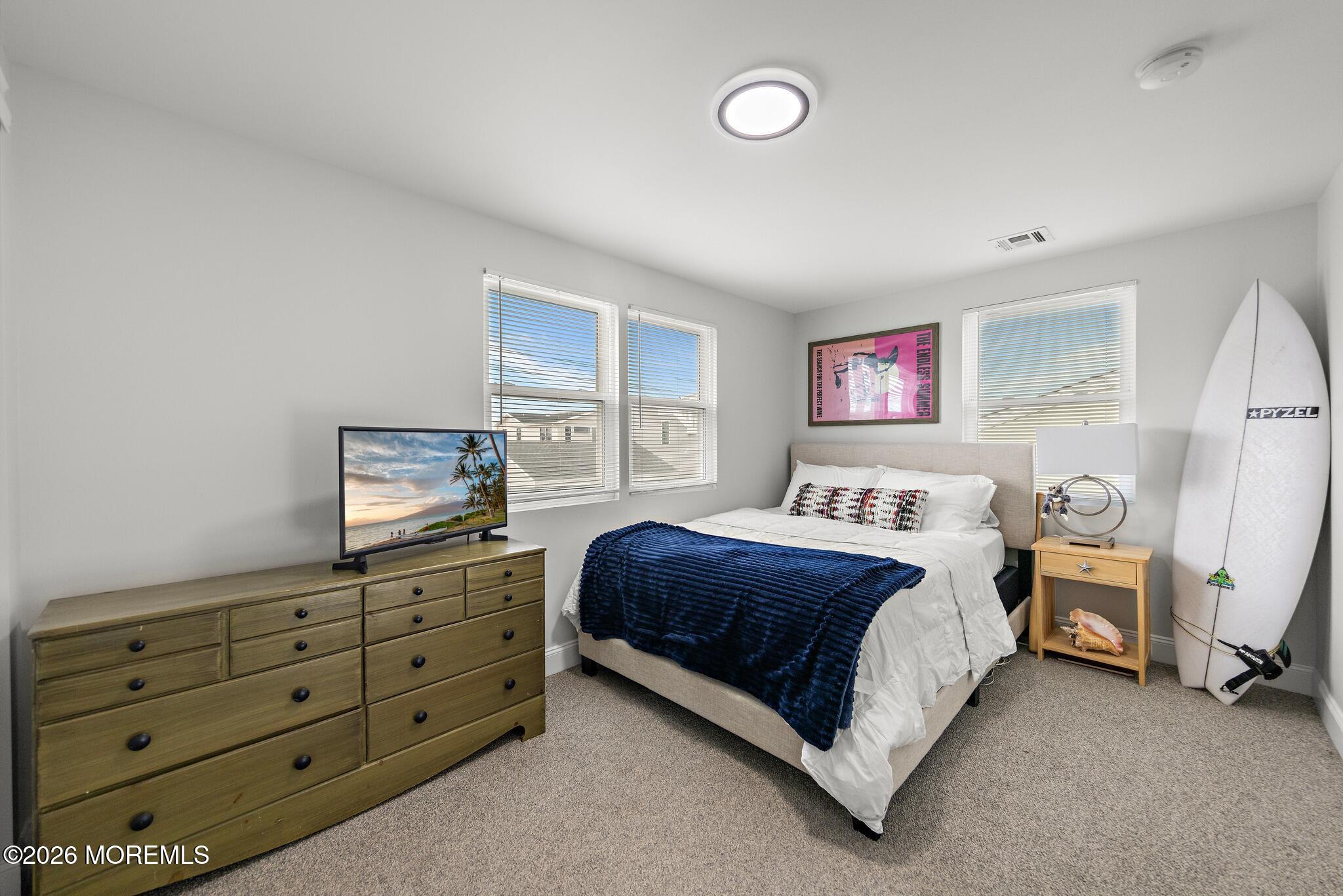 Bedroom with a navy bedspread, wood dresser, and surfboard beside the bed.