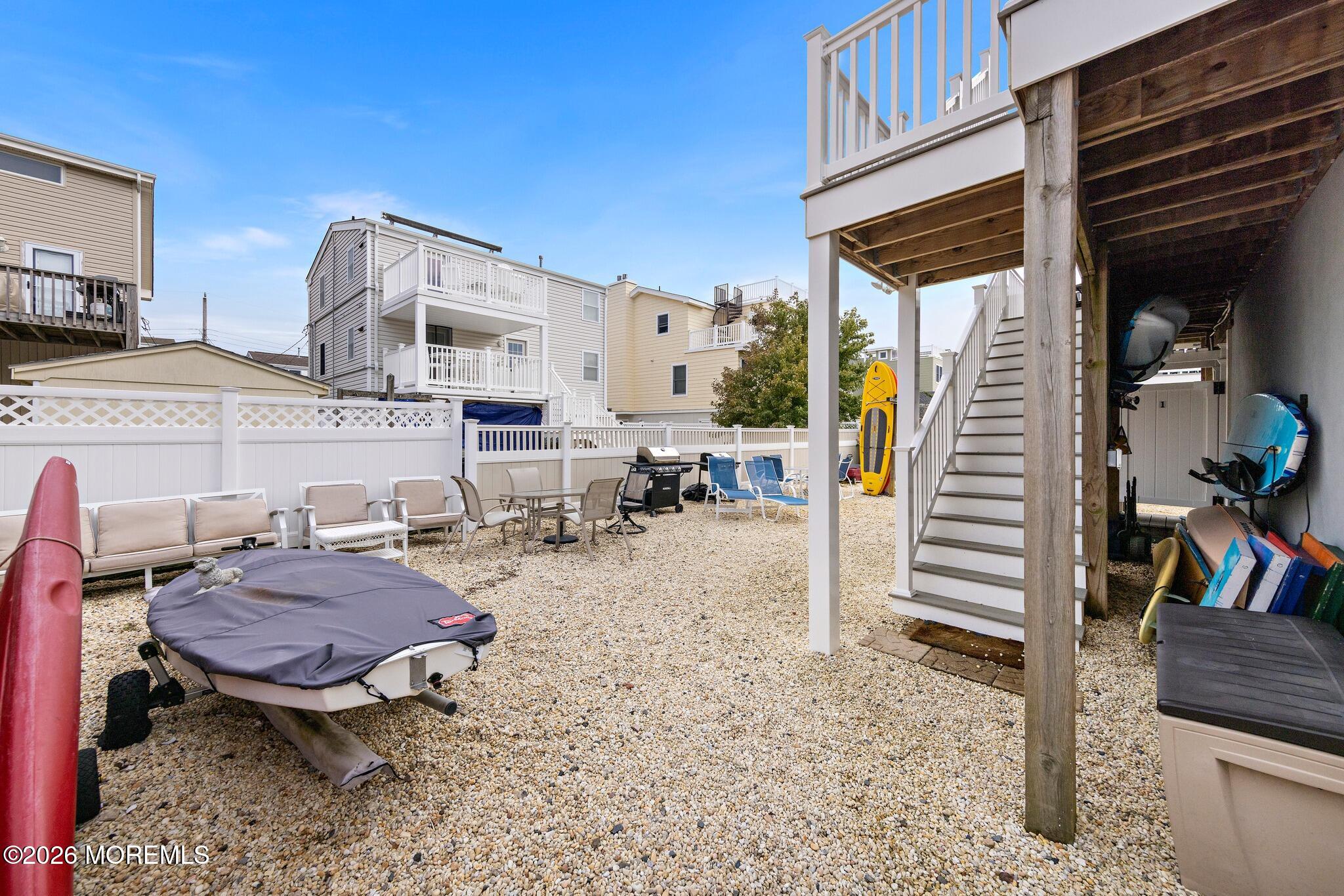 Gravel backyard patio with outdoor seating, a grill, raised deck, and kayaks beside the stairs.