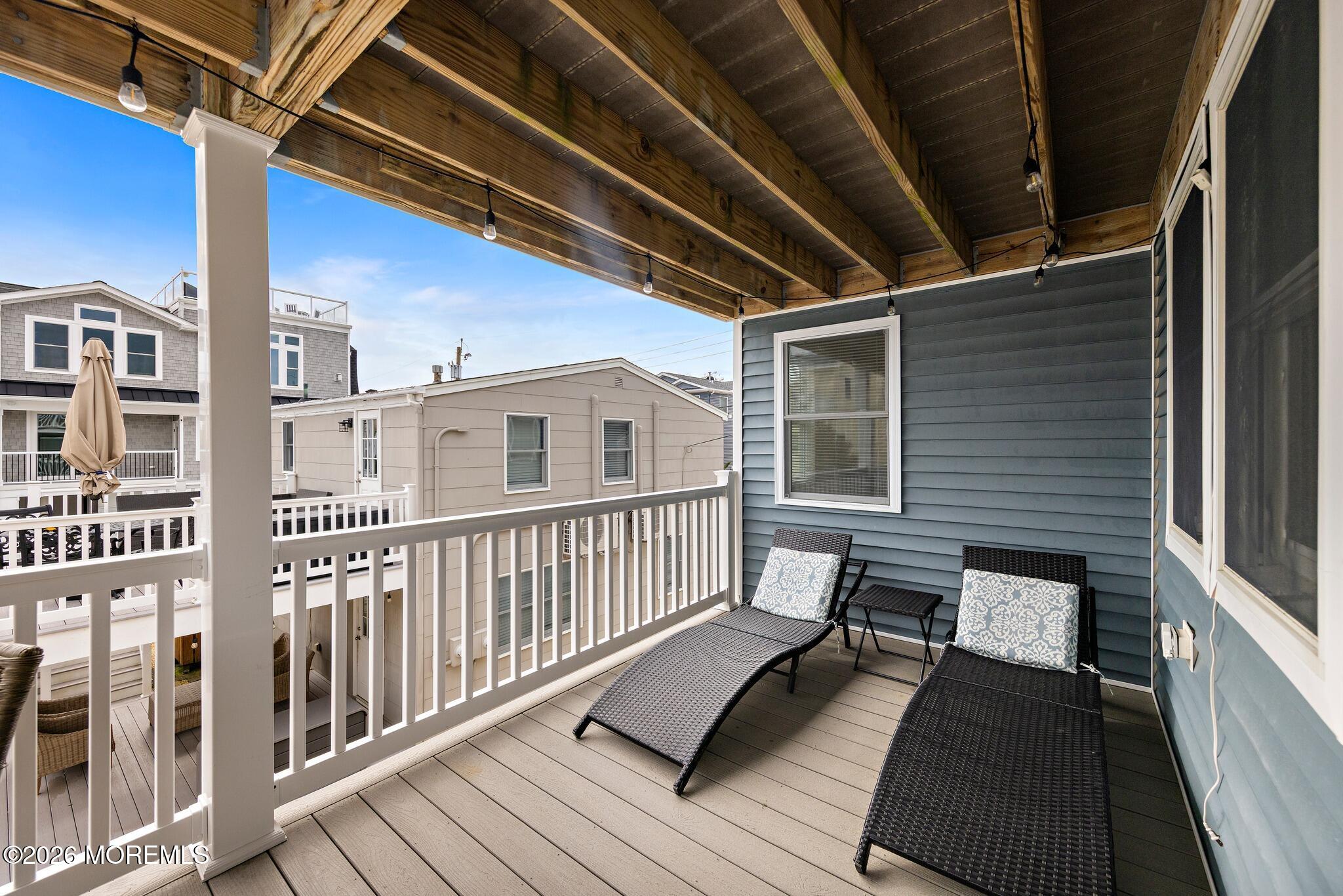 Covered deck with timber ceiling, string lights, and two chaise lounges overlooking neighboring homes.