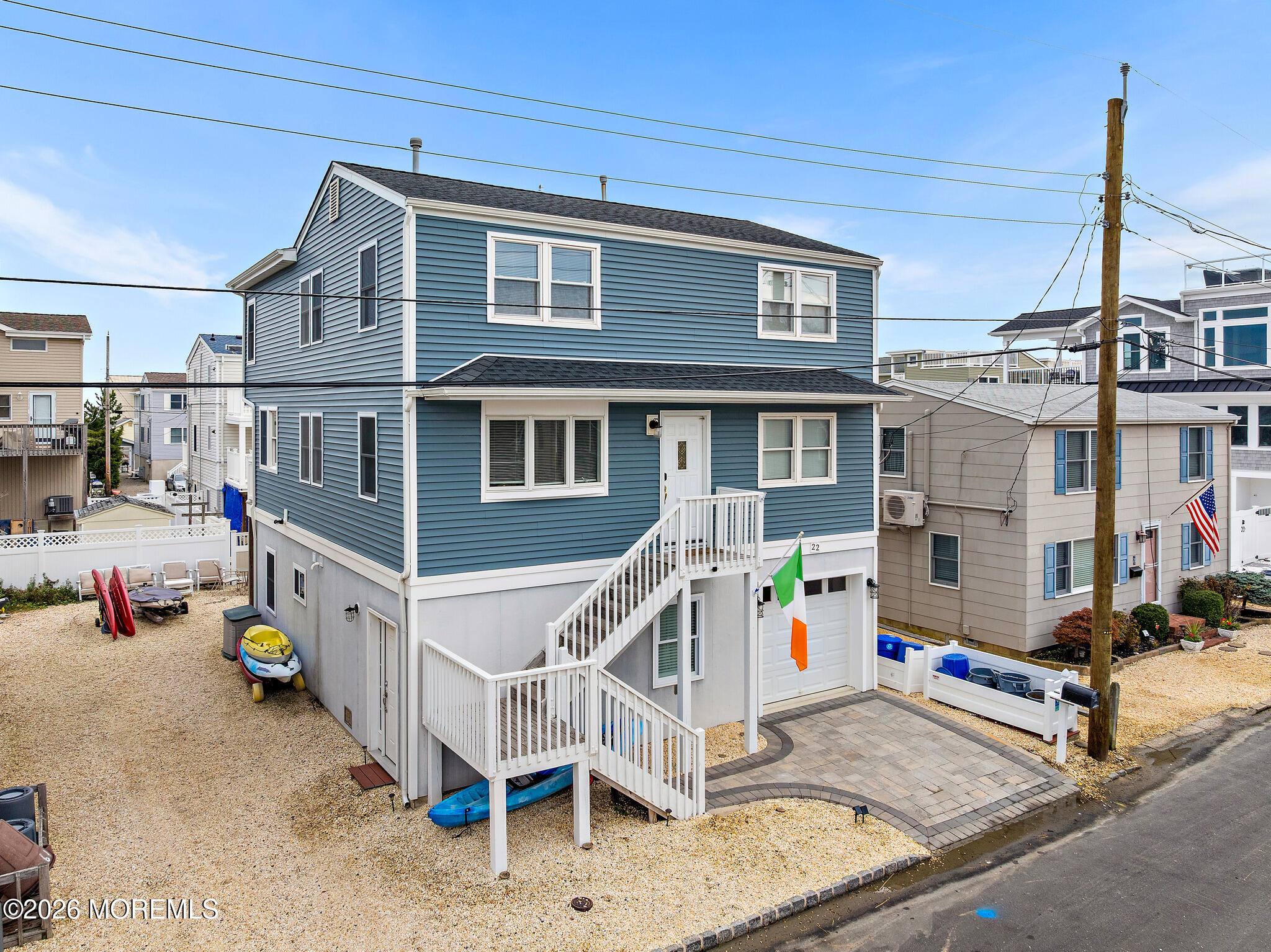 Blue two-story coastal home with white staircase, garage, gravel yard, and kayaks.