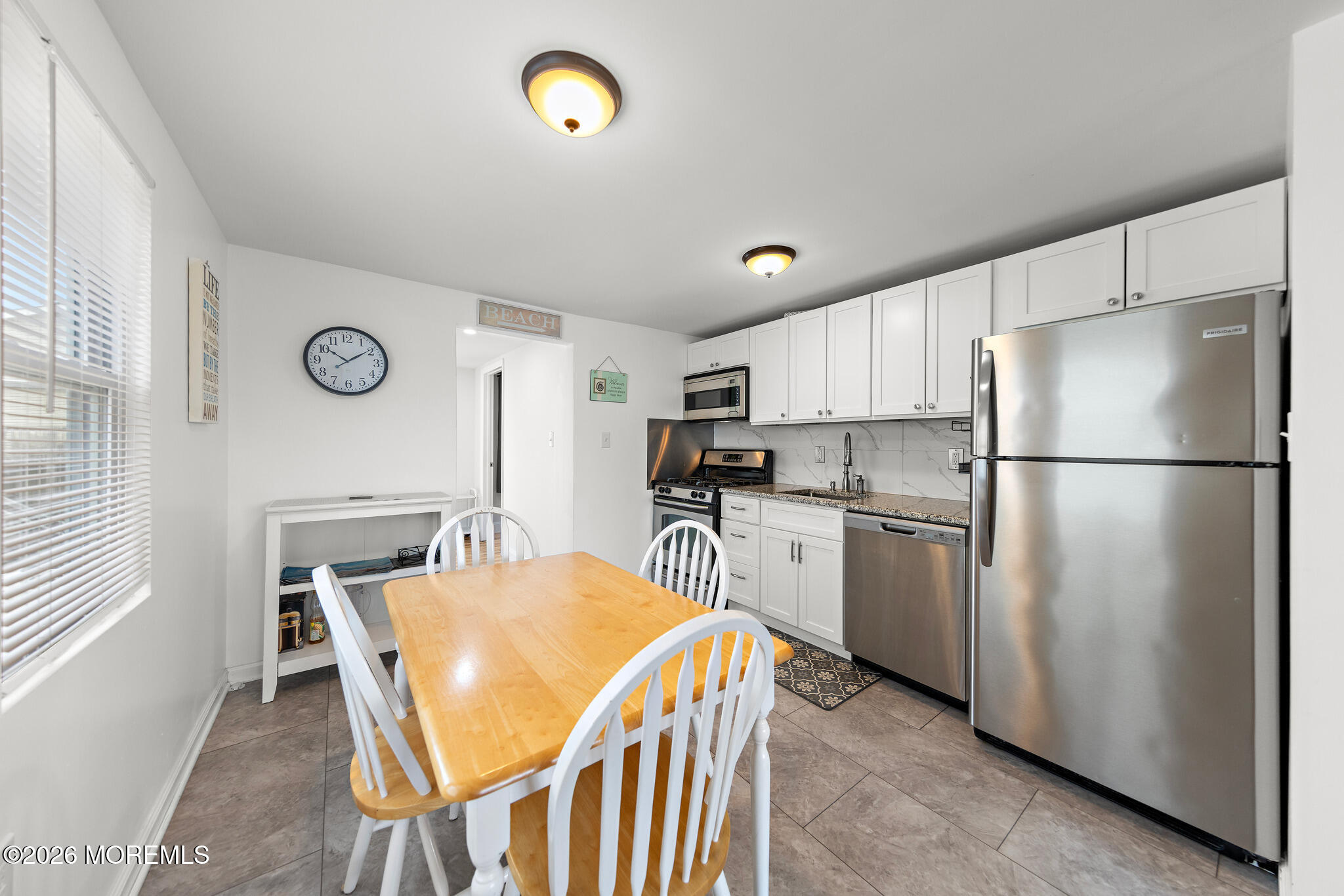 Kitchen with white cabinets, stainless steel appliances, and a wooden dining table with white chairs.
