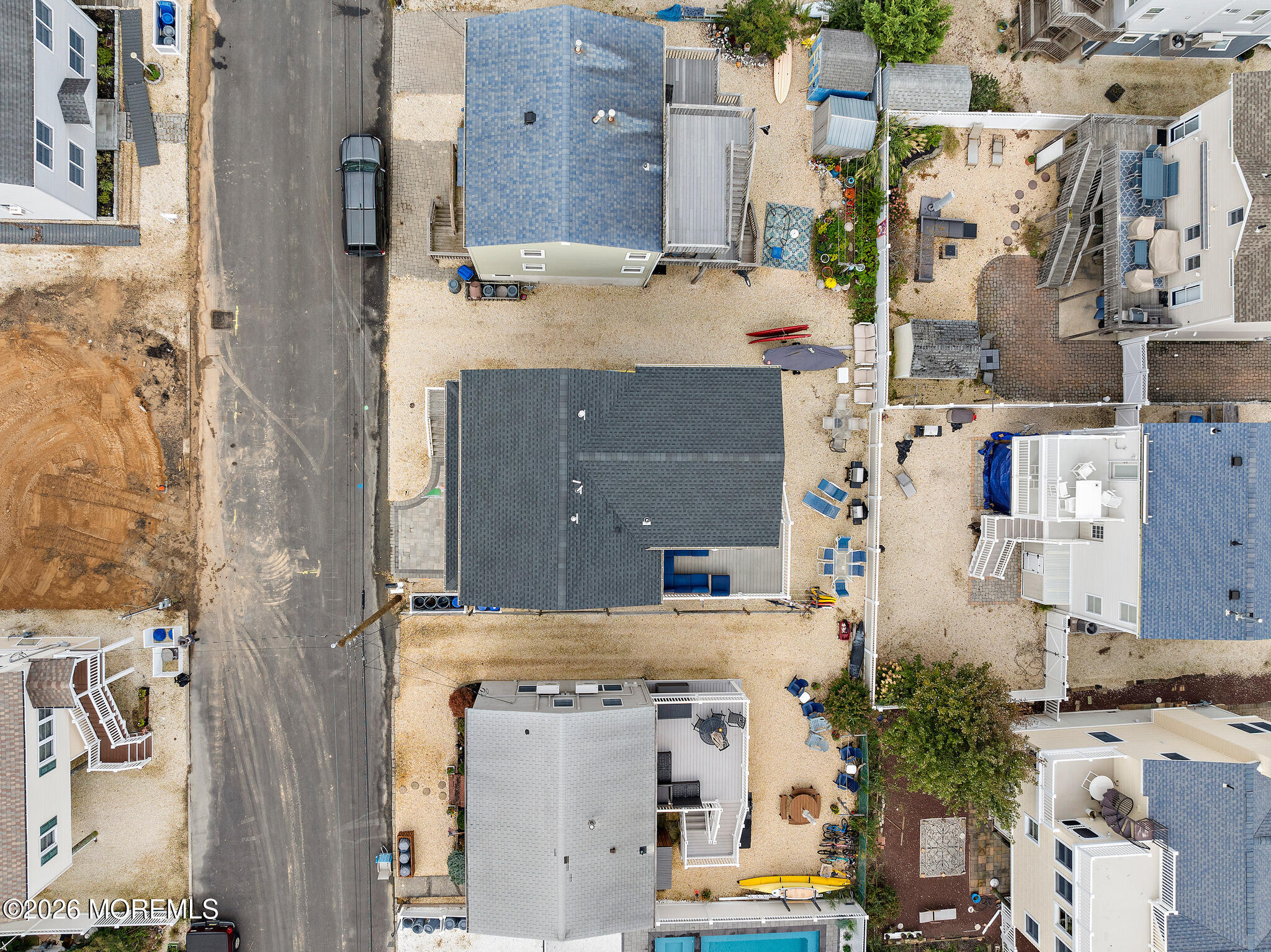 Aerial view of coastal homes with sandy yards, decks, kayaks, and a small pool.