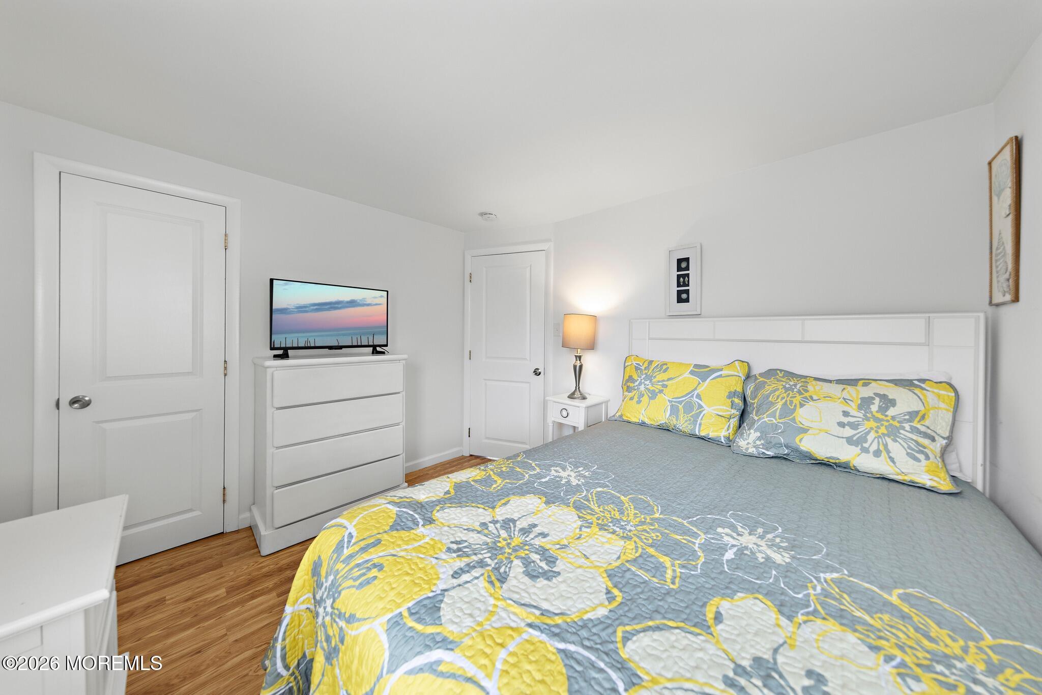 Bedroom with a gray and yellow floral bedspread, white headboard, and television on a dresser.