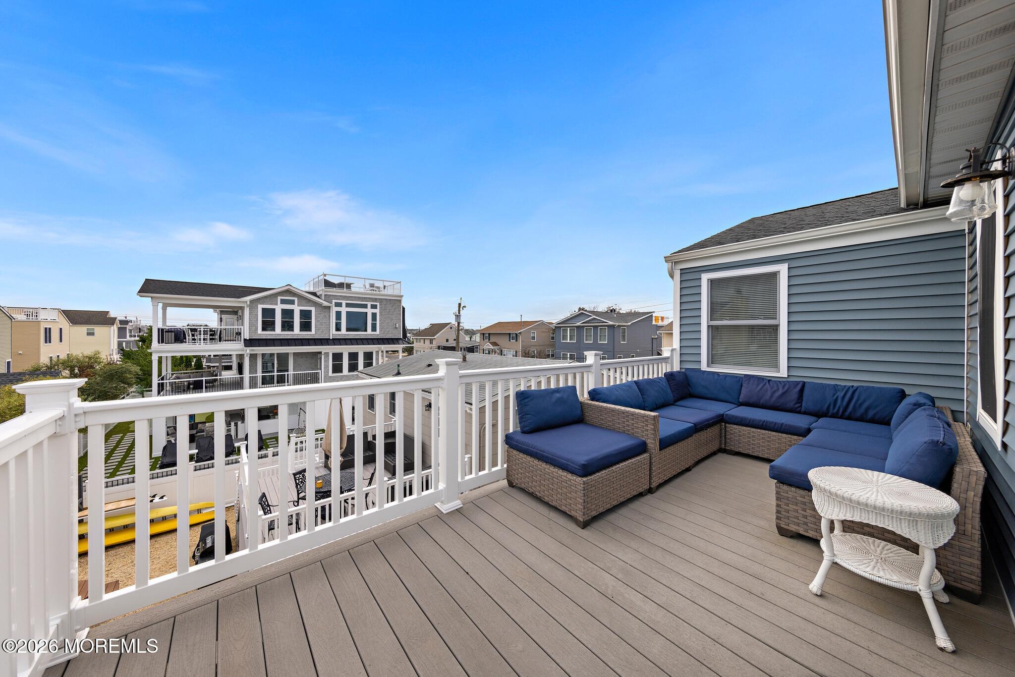 Rooftop deck with navy sectional seating, white railings, and views of neighboring coastal homes.
