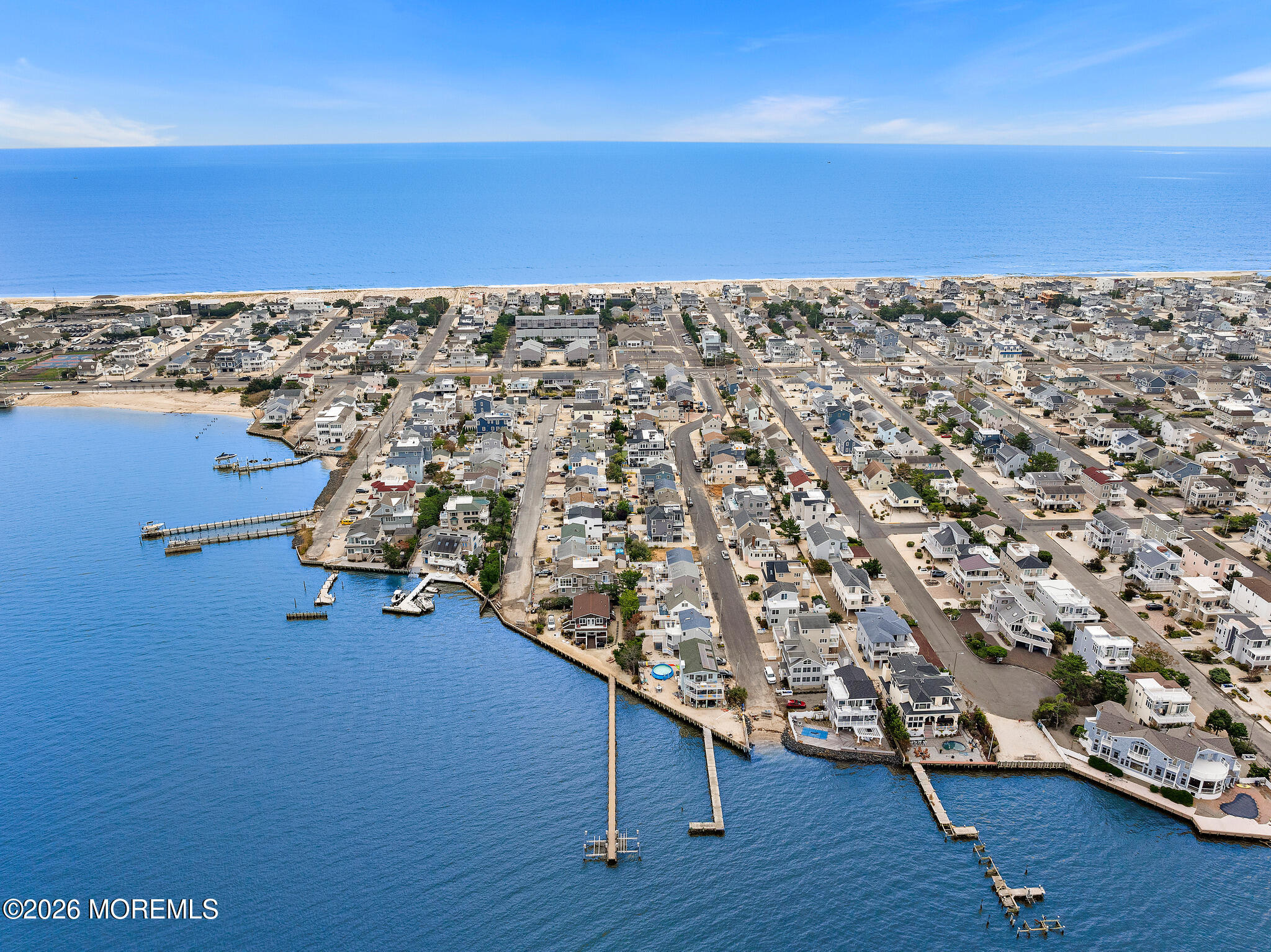 Aerial view of a waterfront neighborhood, with ocean beach, bay, and long residential docks.