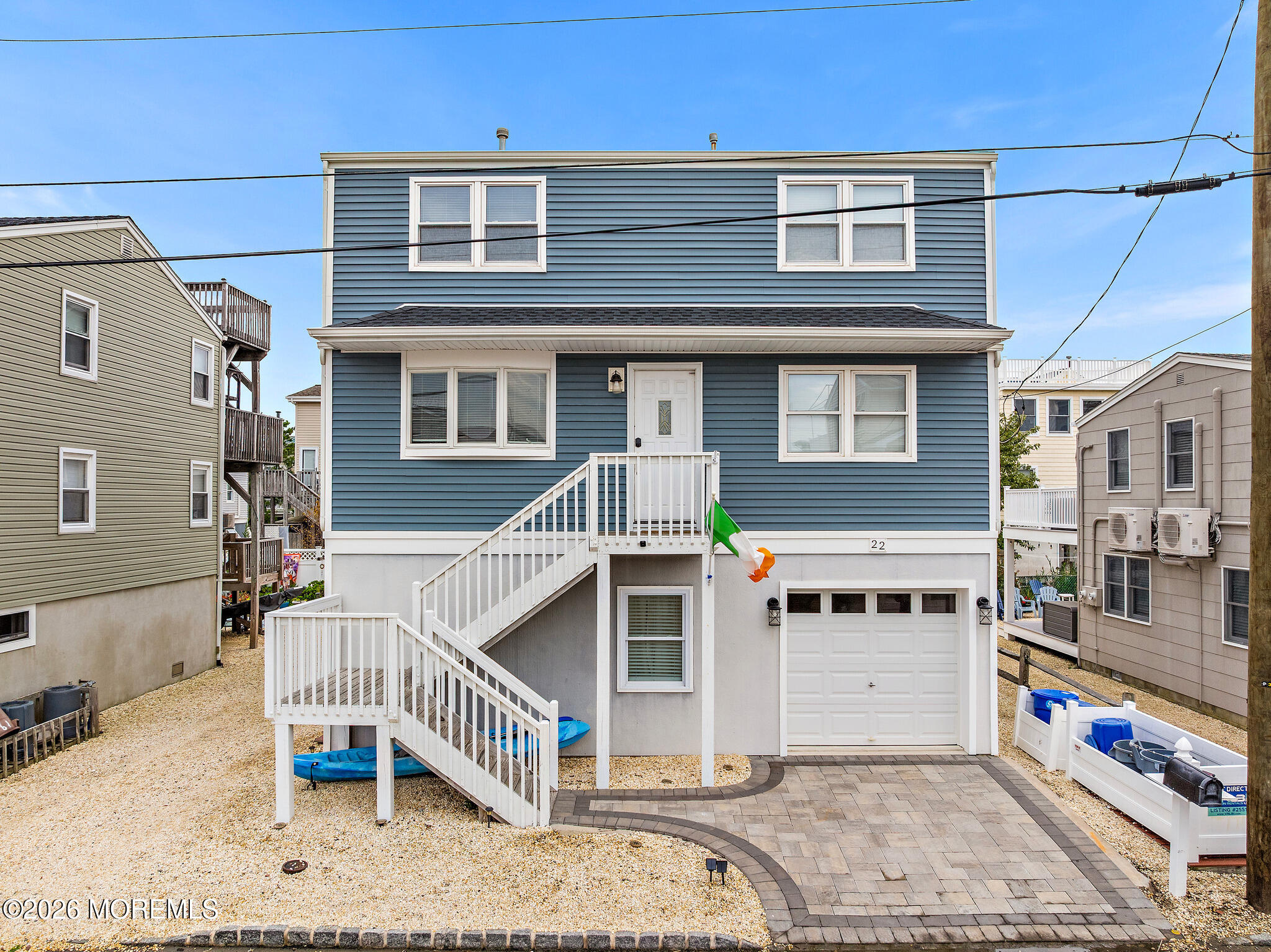 Blue two-story coastal home with white exterior stairs, garage, and paved driveway.