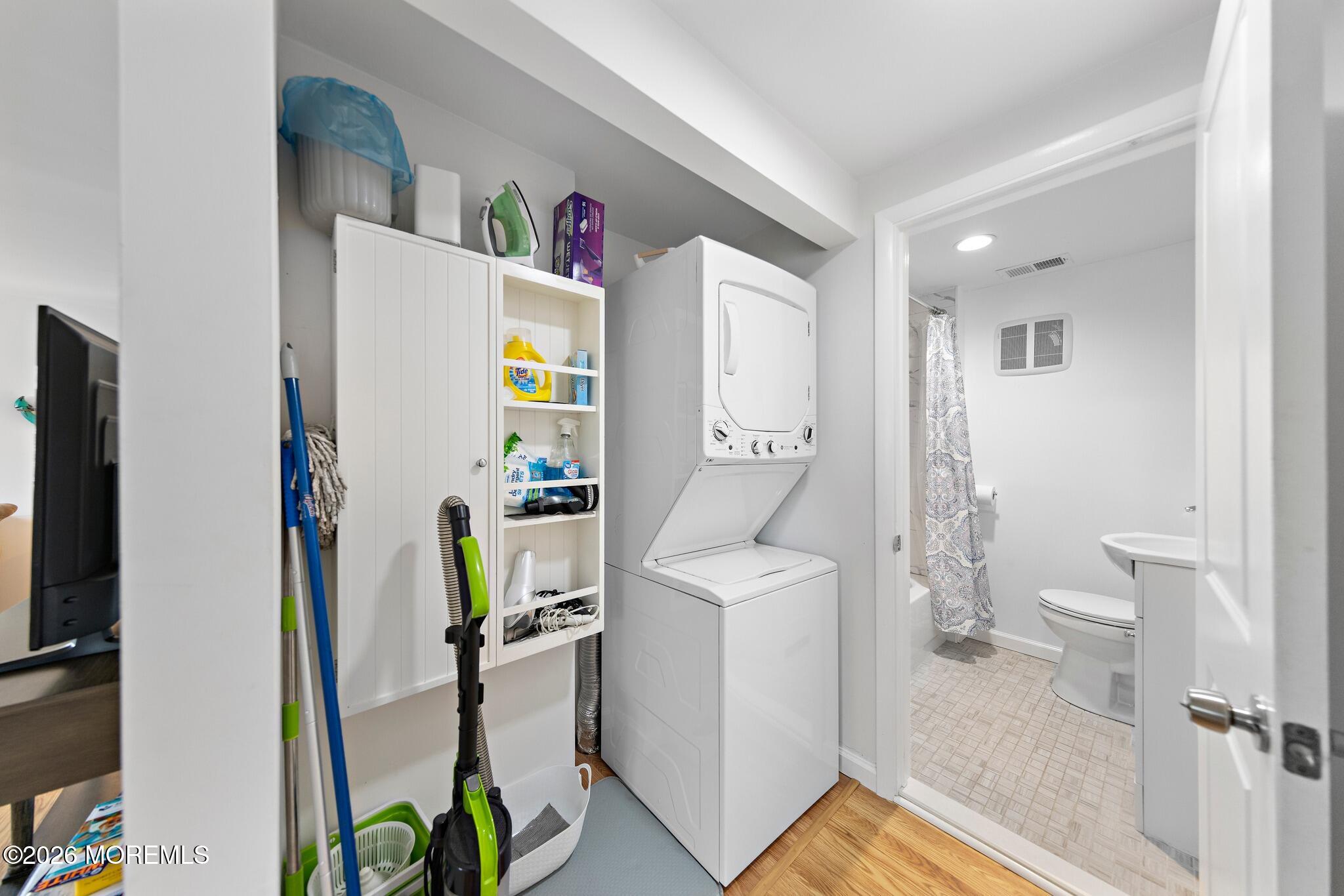 Laundry area with stacked washer and dryer, storage shelves, and an adjoining bathroom.
