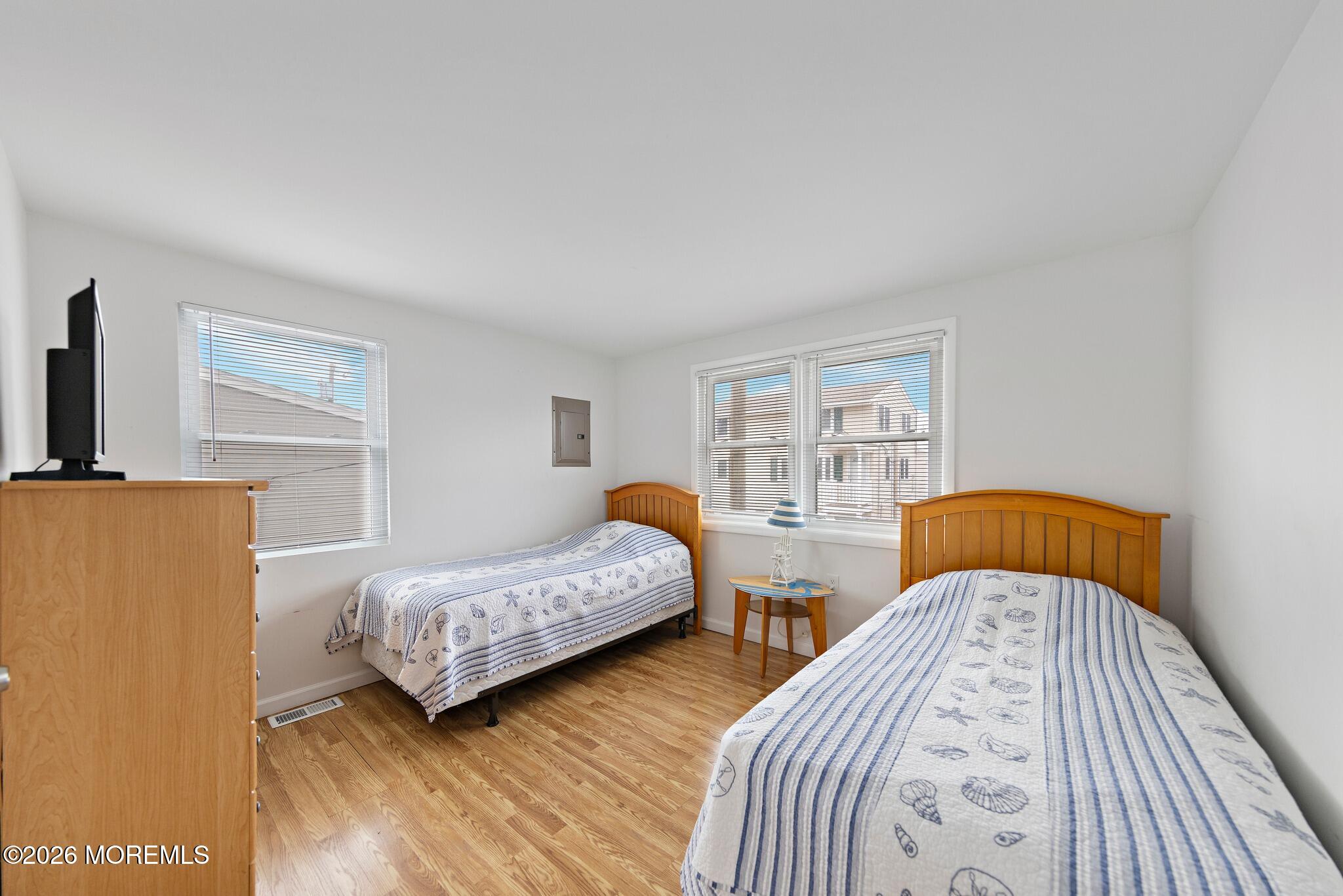 Bedroom with two single beds, seashell-patterned bedding, wood floors, and a small table between the beds.