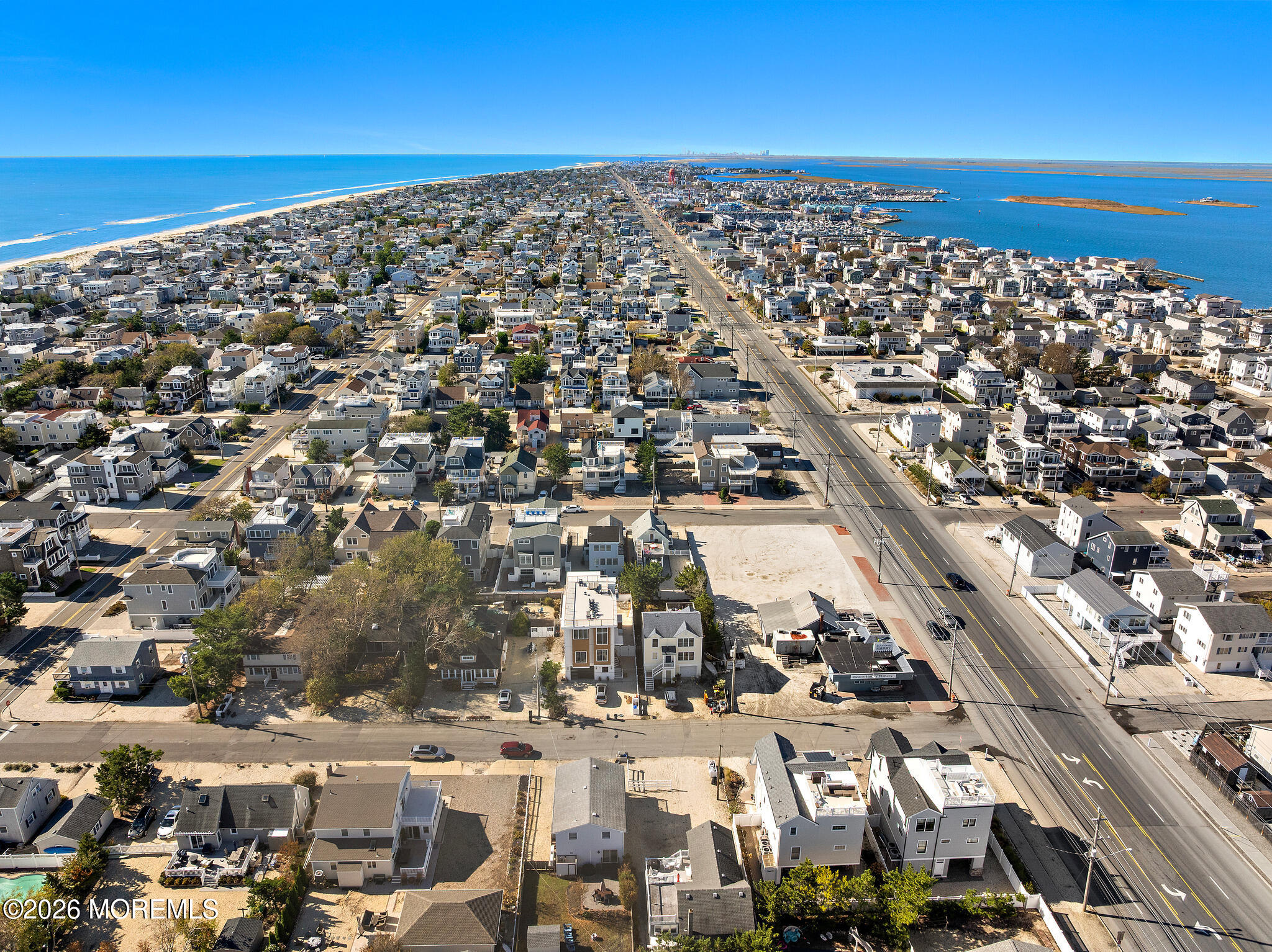 Aerial view of coastal homes between the ocean and bay, divided by a major road.