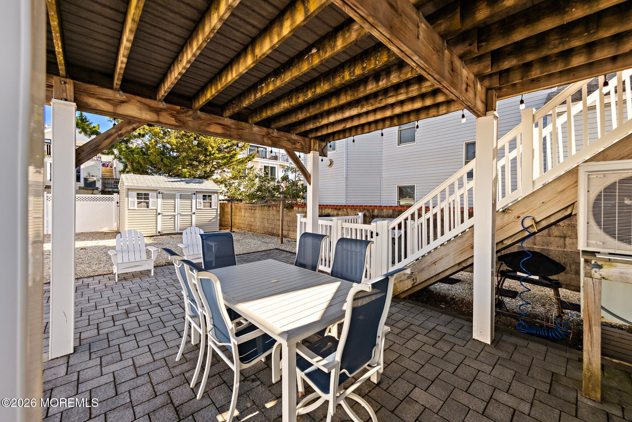 Patio with a timber pergola, outdoor dining set, paver floor, and white staircase.