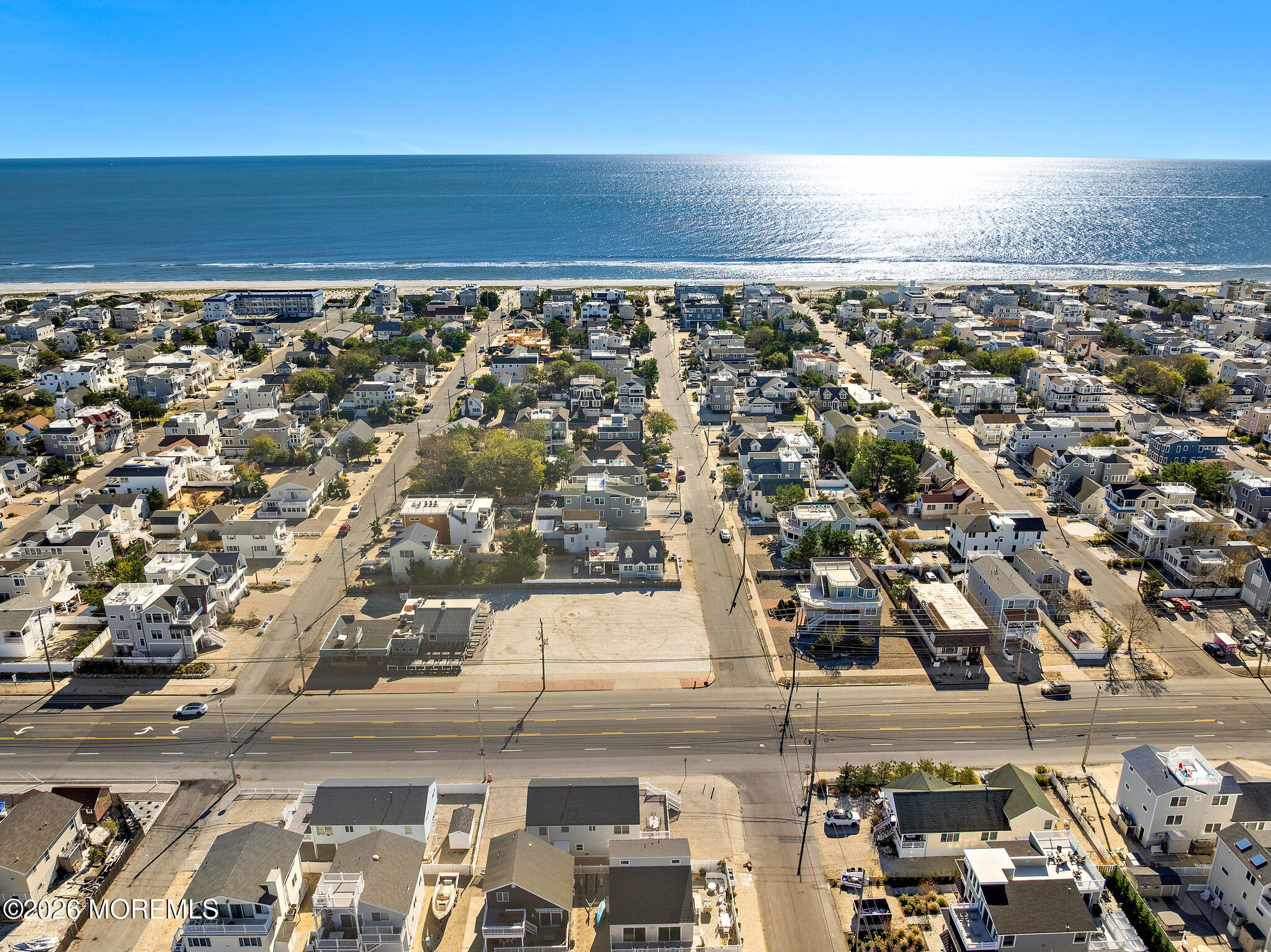 Aerial coastal neighborhood with a large vacant lot, beachfront, and ocean beyond.