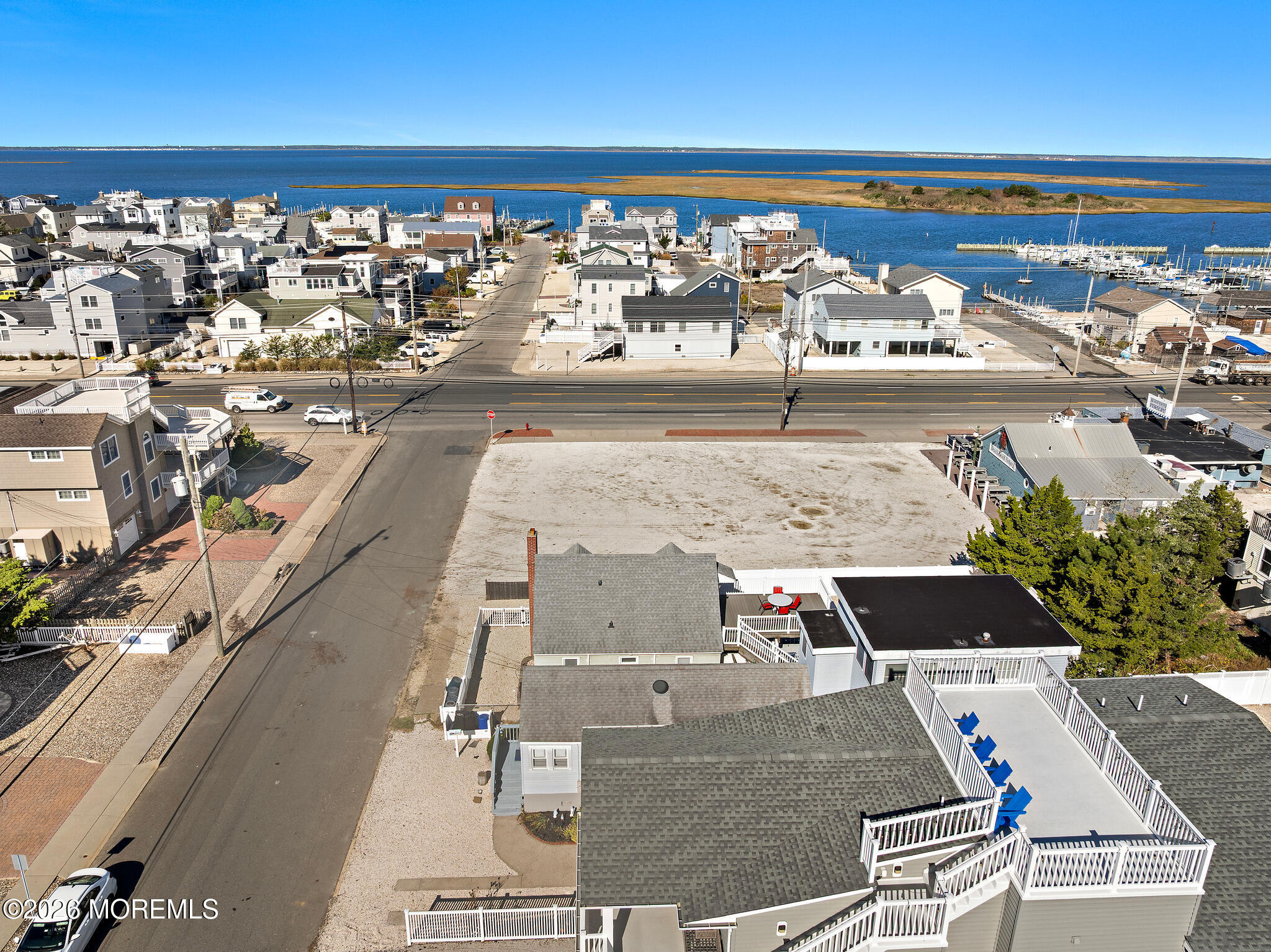 Aerial view of coastal homes beside a bay, marina docks, and a large vacant lot.
