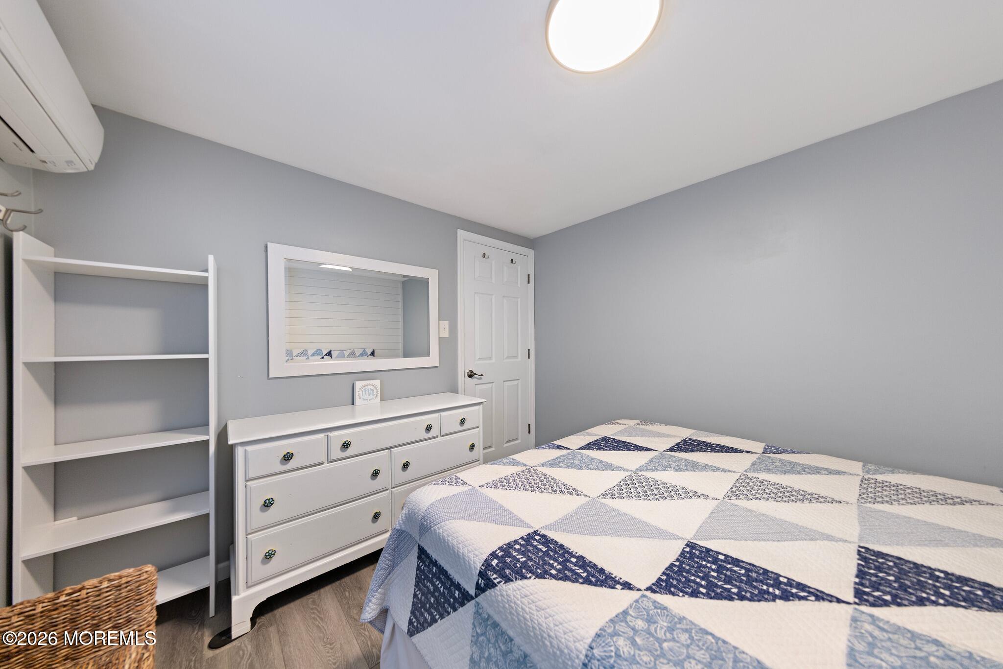 Bedroom with a blue-and-white patchwork quilt, white dresser, mirror, and open shelving.