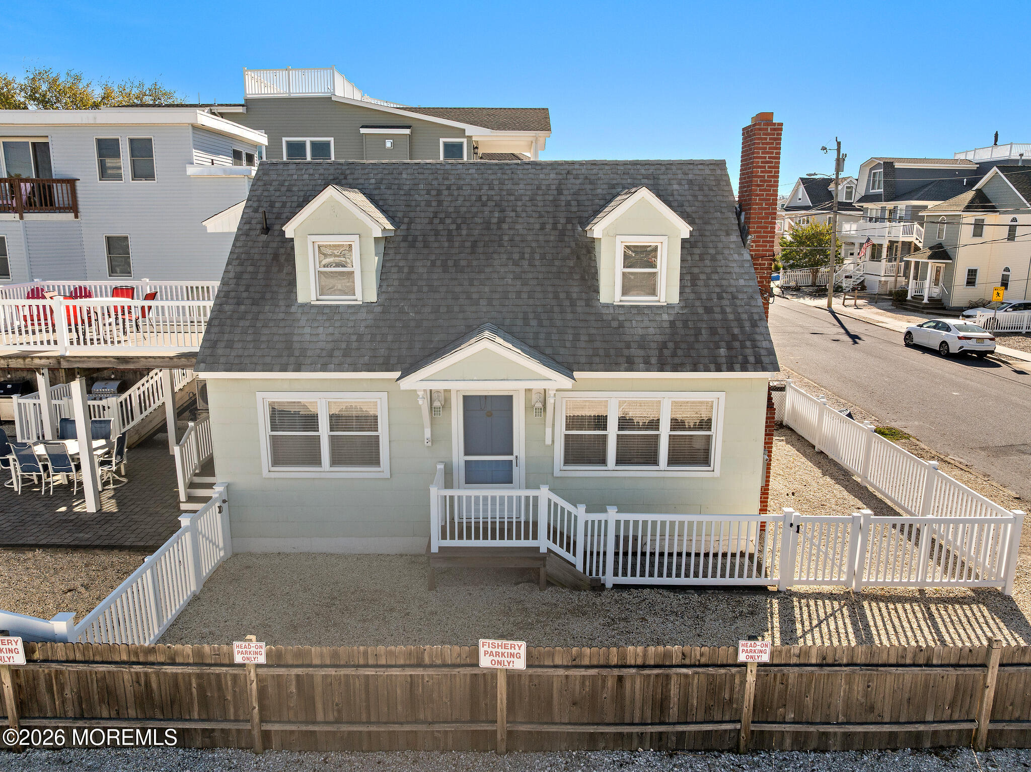Coastal house with twin roof dormers, white fencing, and a gravel yard.