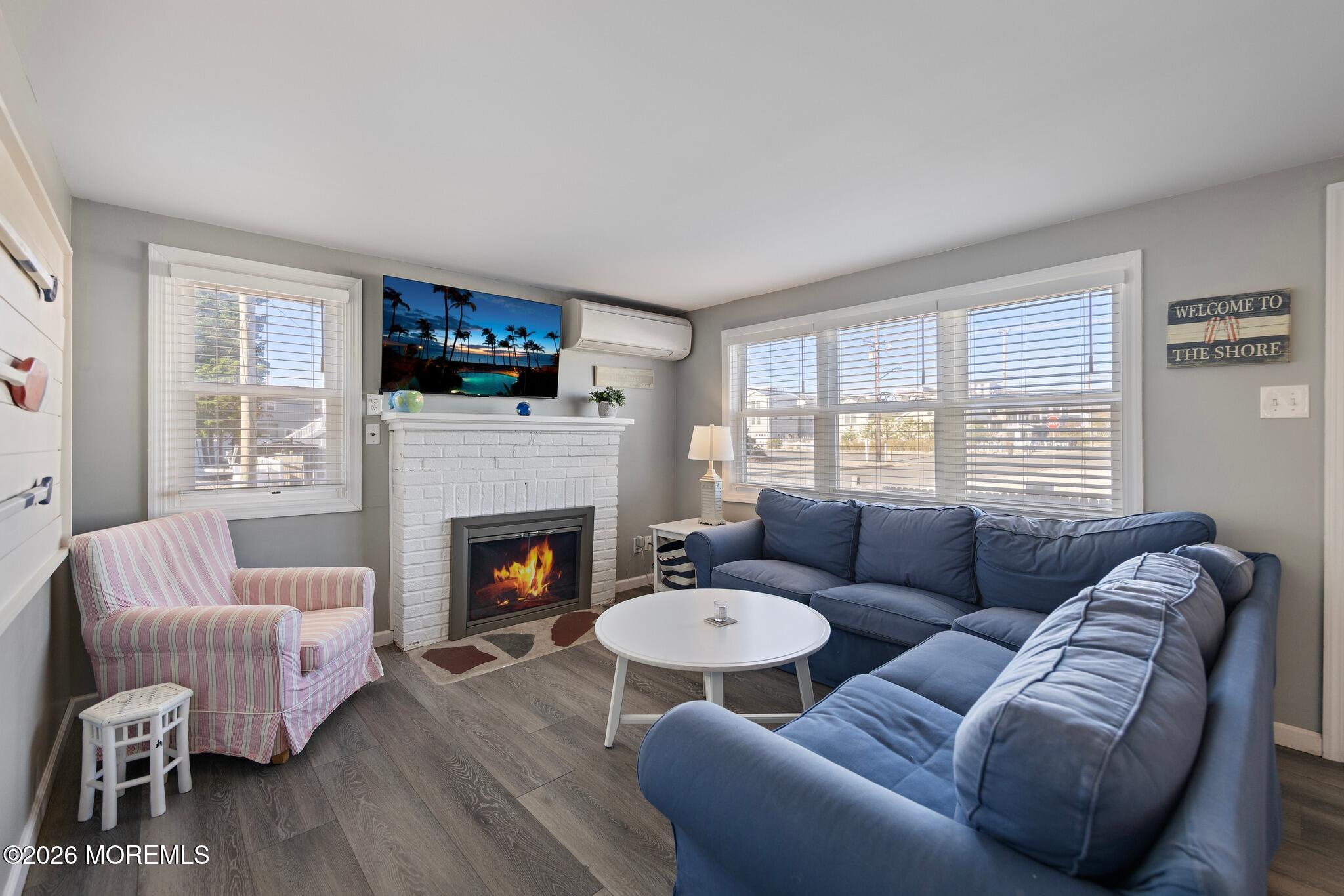 Furnished living room with blue sectional, white brick fireplace, and large shuttered windows.
