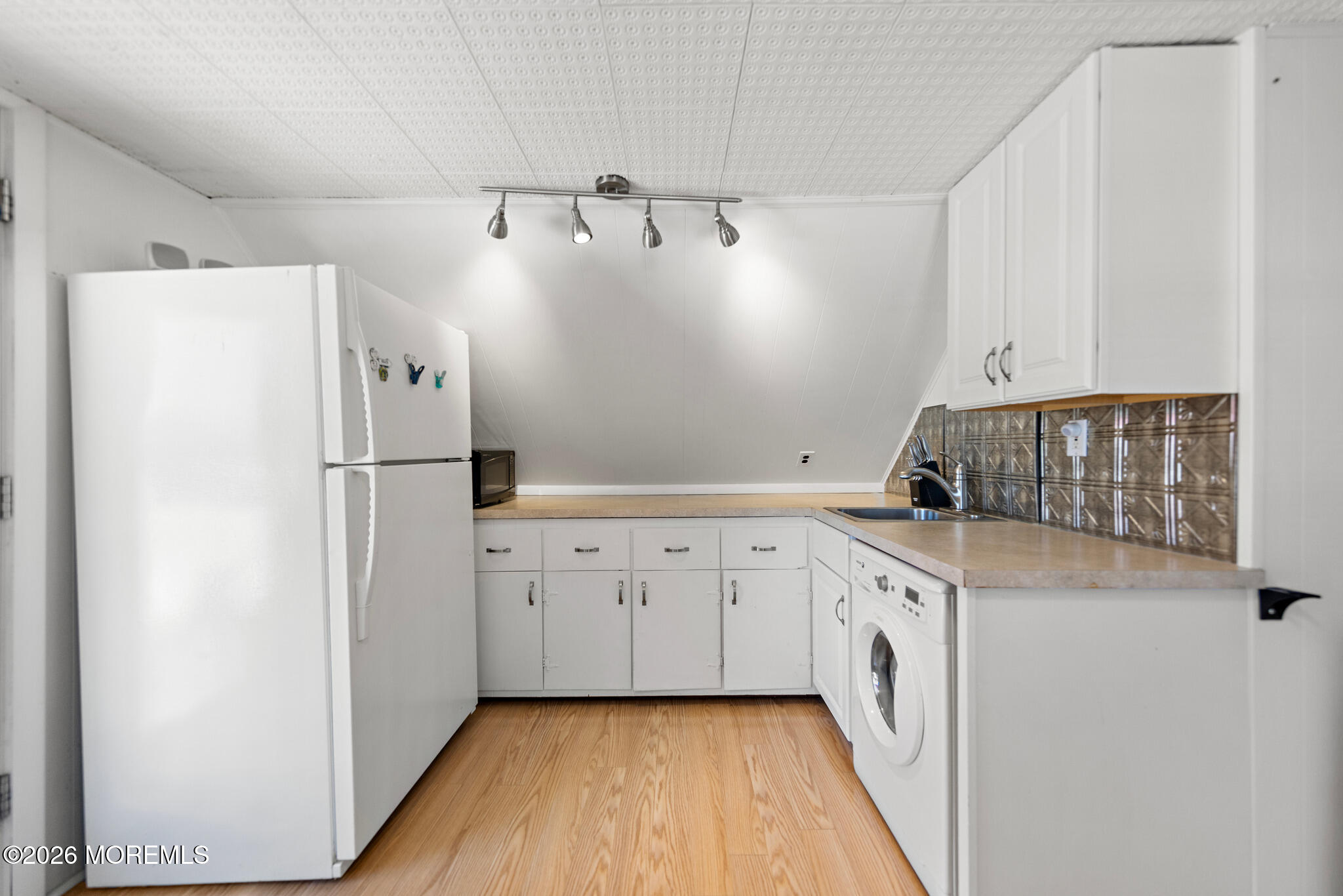 Compact kitchen with white cabinets, dark tile backsplash, and a front-loading washer.