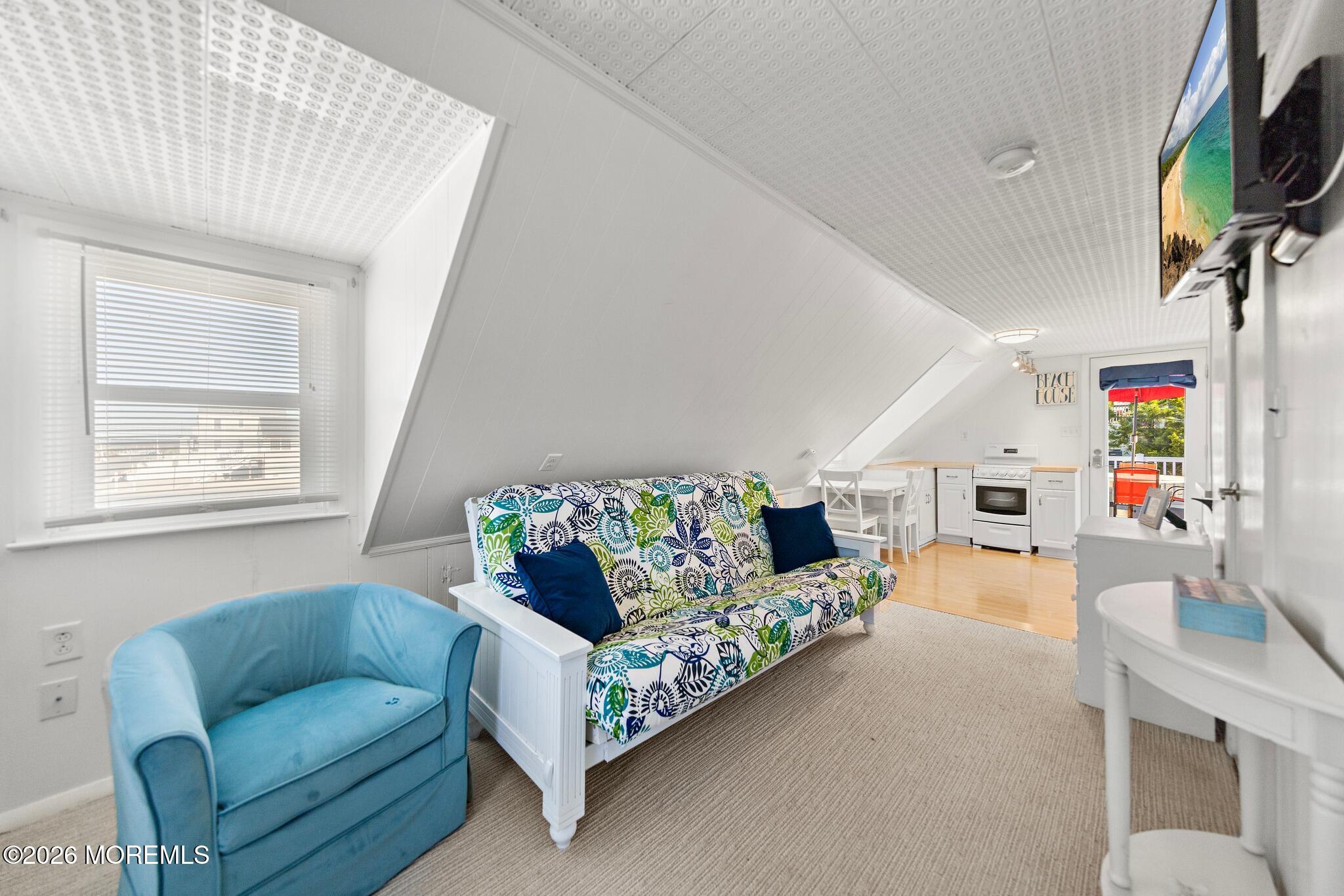 Attic living room with a patterned futon, blue armchair, and compact kitchenette.