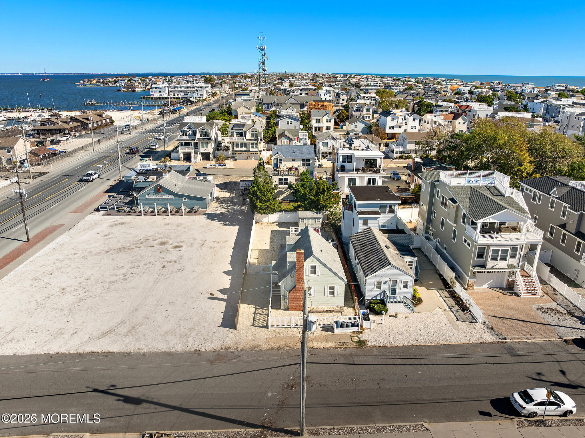 Aerial view of a sandy vacant lot among coastal homes, with water visible in the distance.