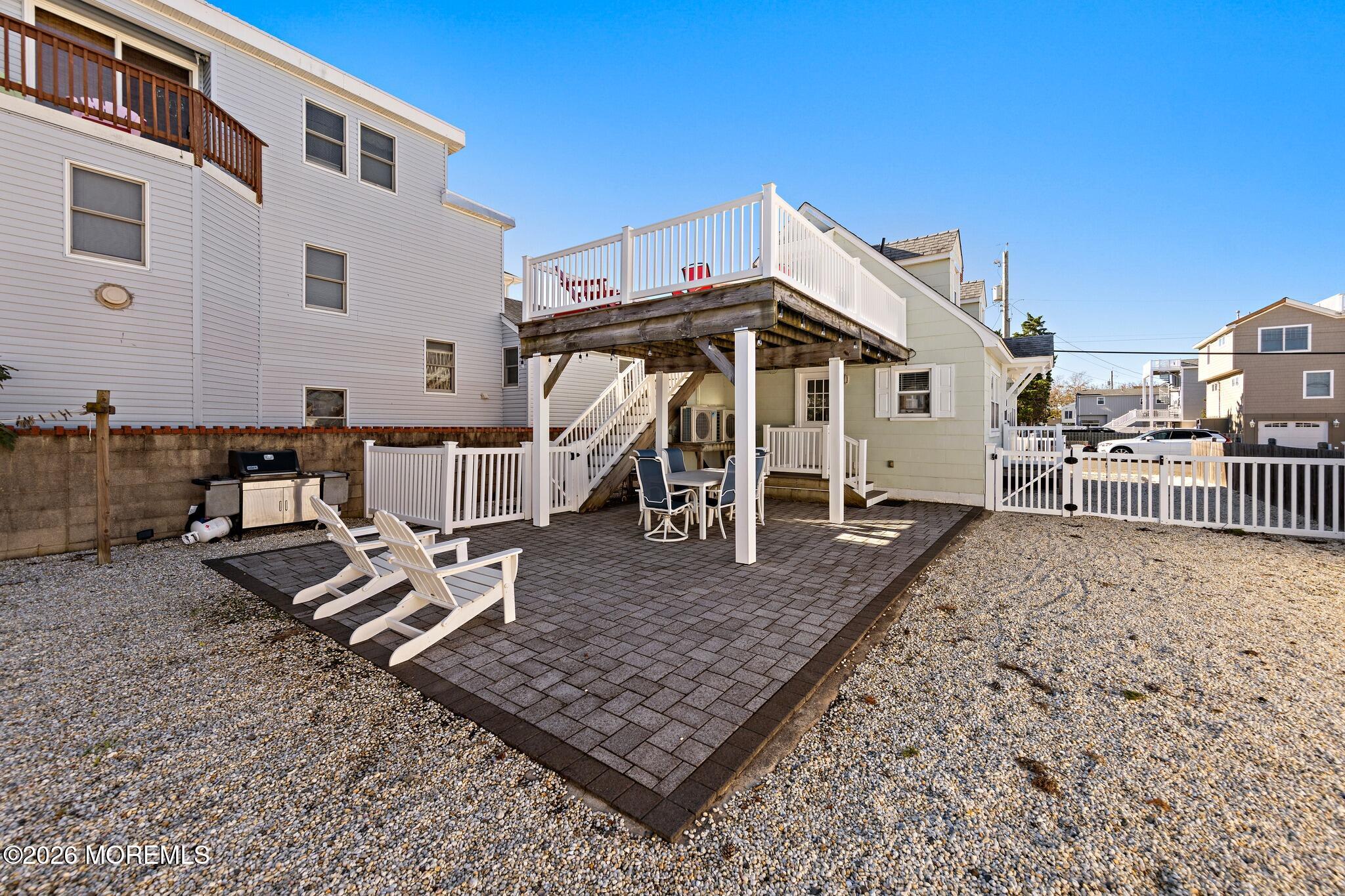 Backyard patio with Adirondack chairs, a dining set under an elevated deck, and a grill.