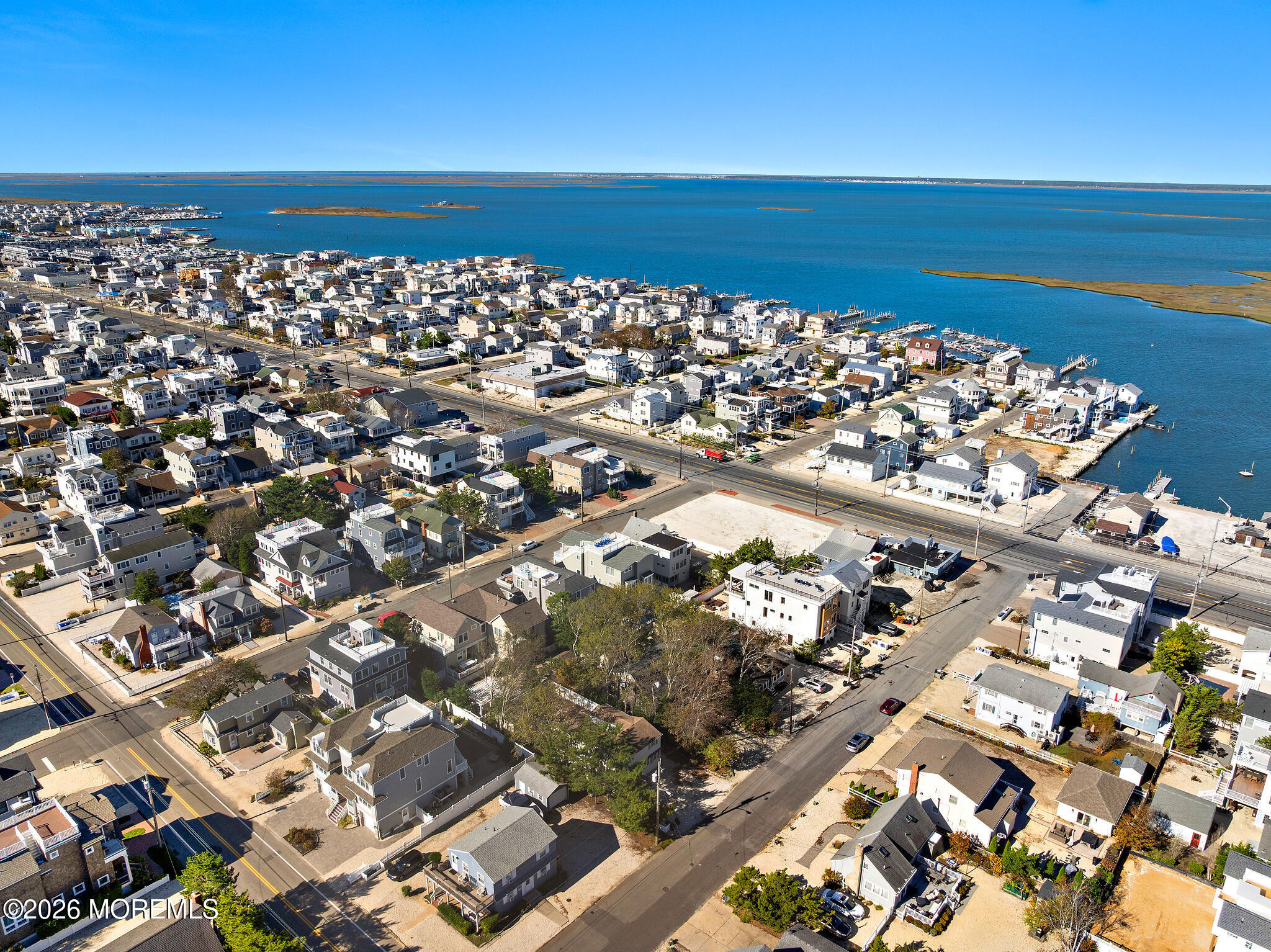 Aerial view of a coastal neighborhood beside a blue bay, with docks and marsh islands.