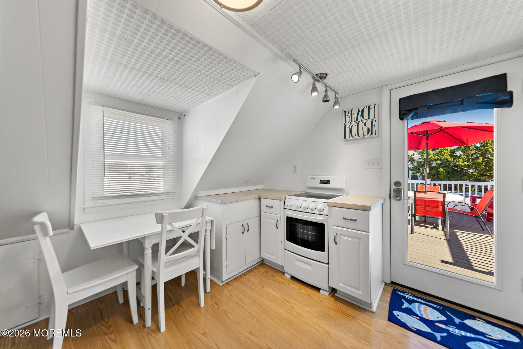 Compact white kitchen with a sloped ceiling and an open door to a sunny deck.