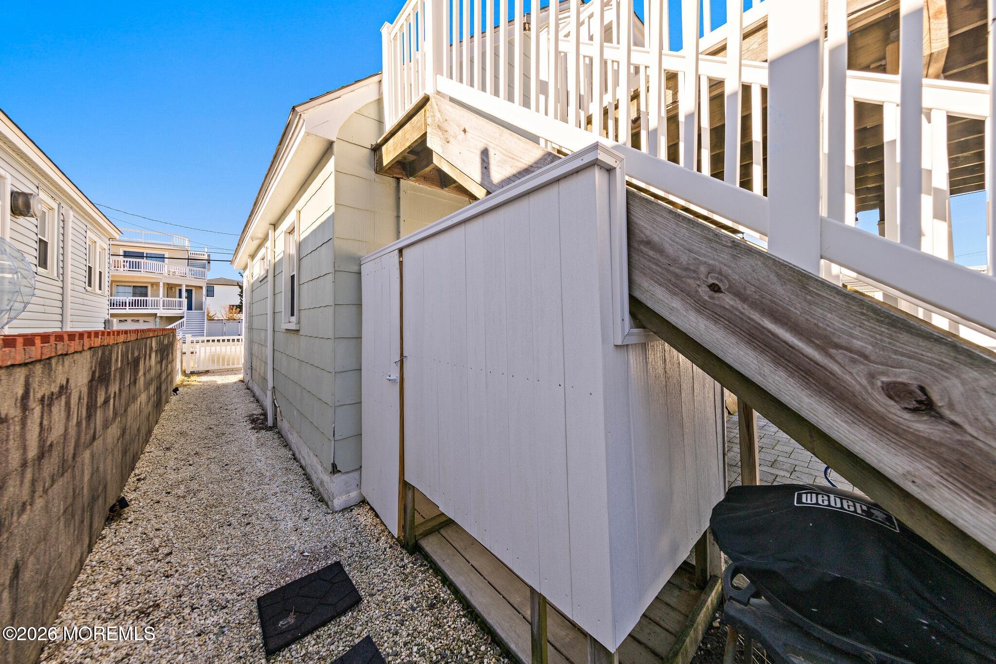 Side passage with a gravel path, storage shed beneath the stairs, and covered grill.