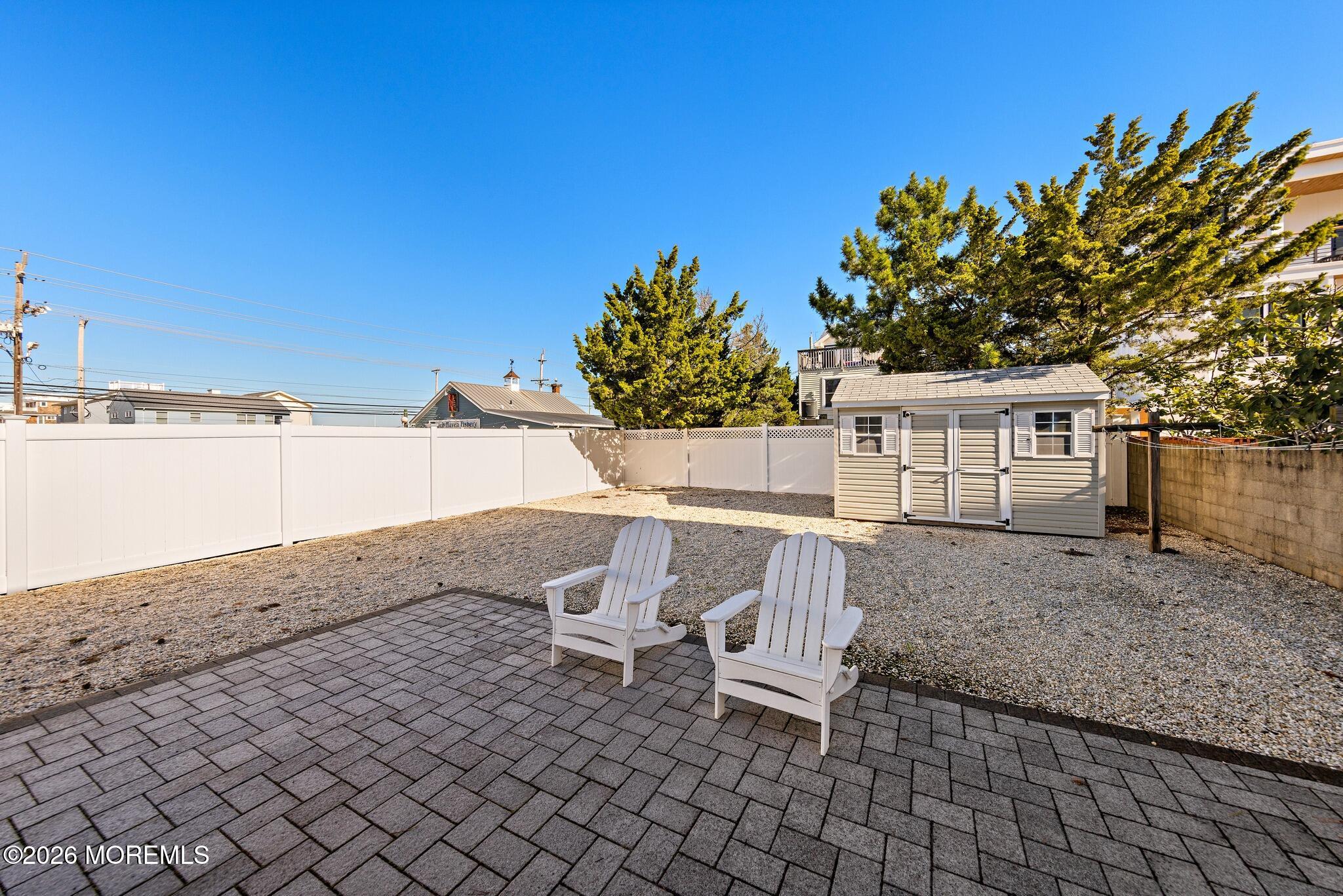 Fenced backyard with a paver patio, two white Adirondack chairs, gravel yard, and storage shed.