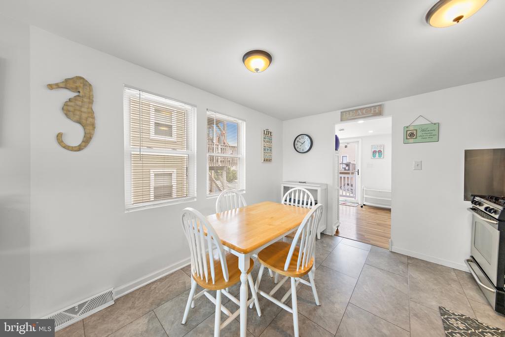 Dining area with a wooden table, white chairs, and two windows with blinds.